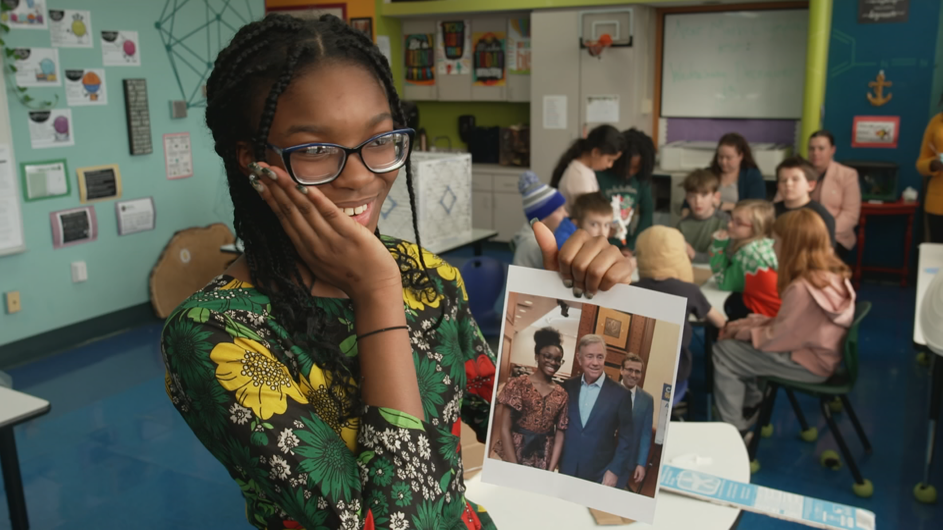 Eniola Shokunbi steht in einem Klassenzimmer und hält ein Bild von sich und Gouverneur Ned Lamont in der Hand.