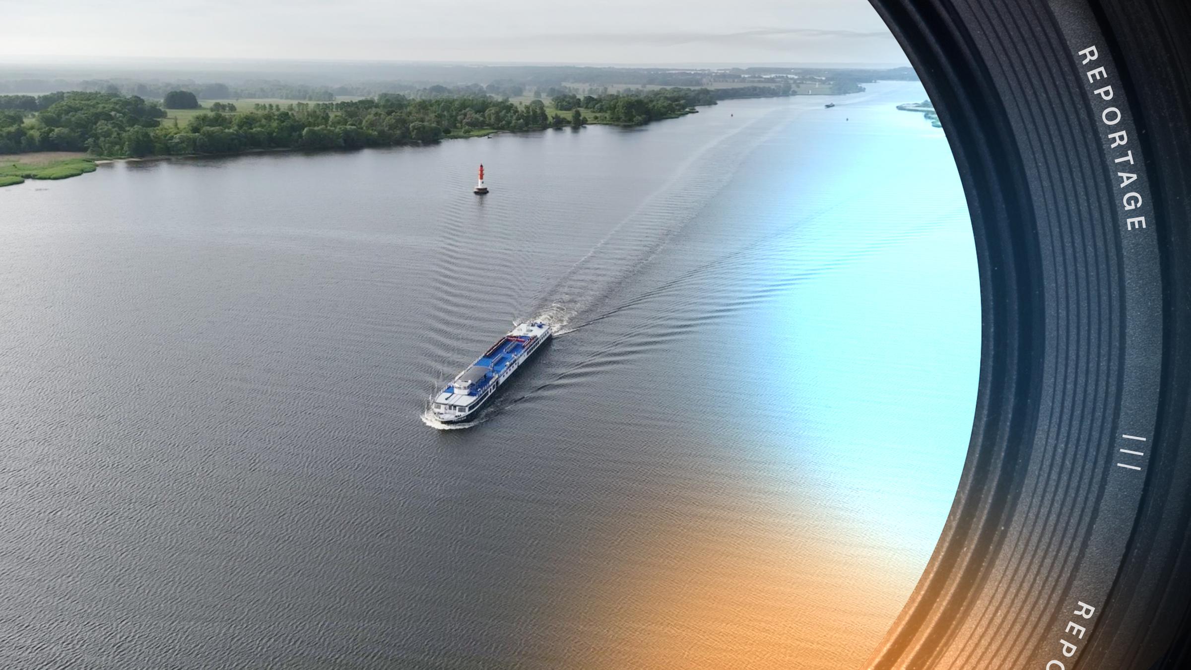 Ein weiter Fluss, auf dem ein Schiff fährt. Im Hintergrund eine flache grüne Landschaft.