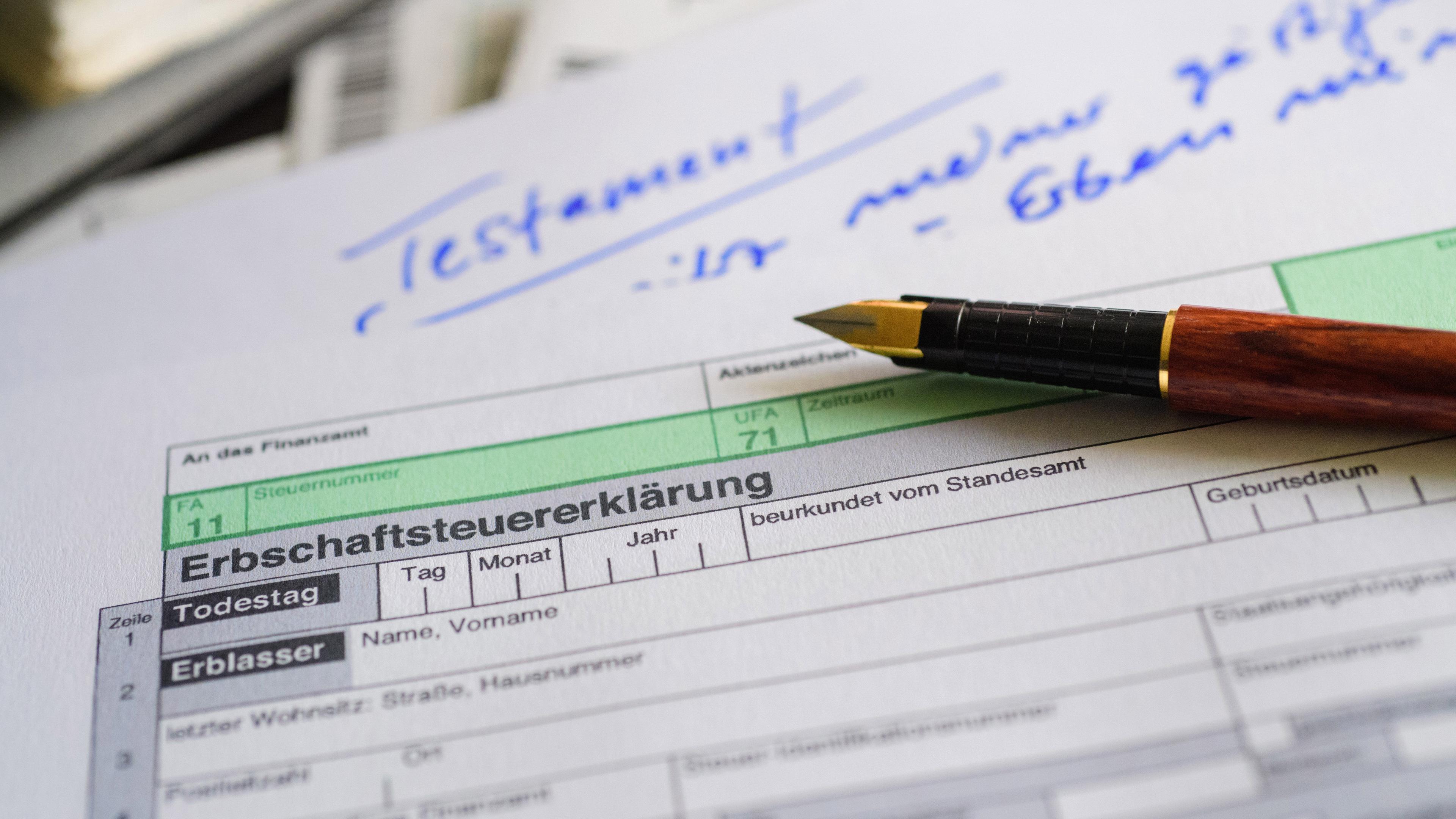 Ein Formular für die Erbschaftsteuererklärung sowie Stift und Testament liegen auf einem Tisch.