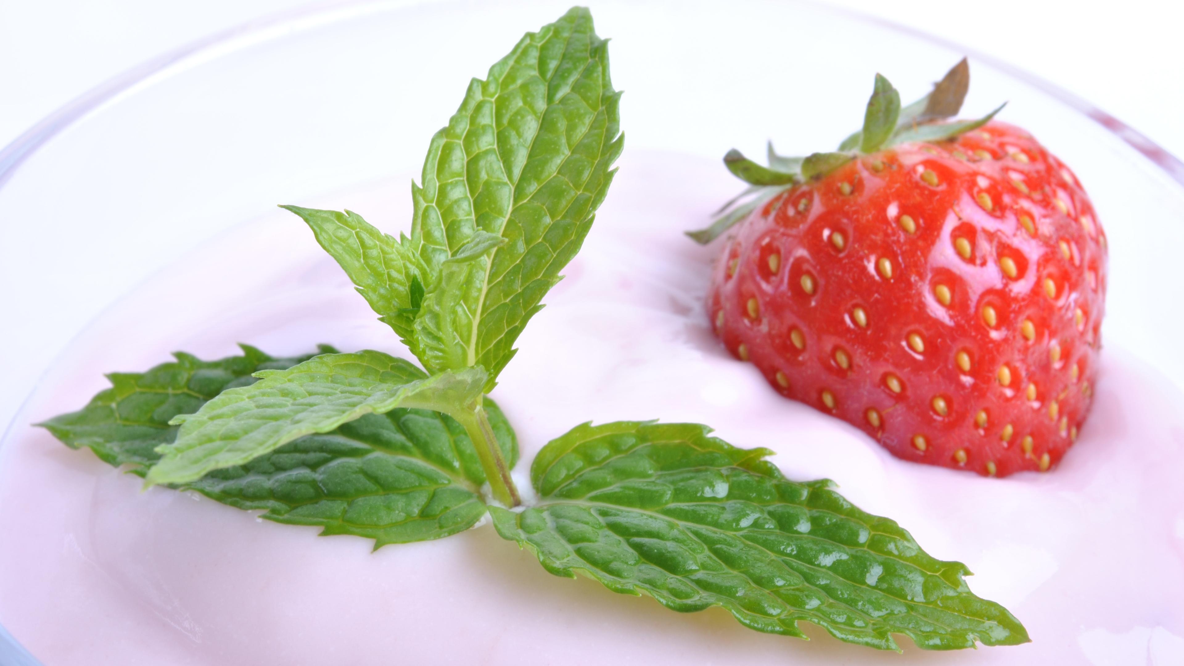 Ein Glas mit Erdbeerjoghurt garniert mit einer Erdbeere und Minzblättern.