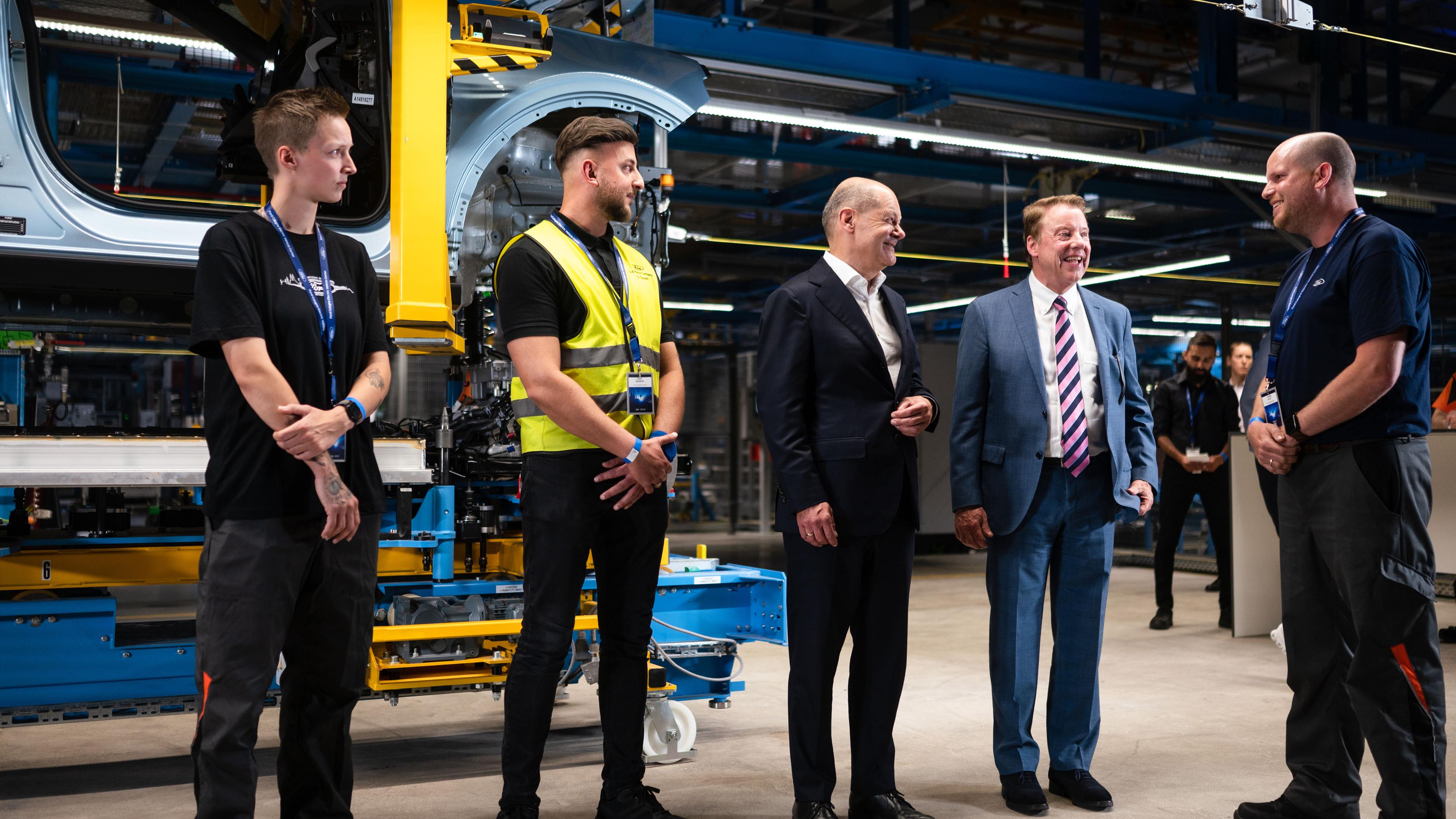 Nordrhein-Westfalen, Köln: Bundeskanzler Olaf Scholz (3.v.l, SPD) und William Clay Ford, Vorstandsvorsitzender von Ford, sprechen bei der Vorab-Eröffnungsfeier des Ford Cologne Electric Vehicle Center mit Mitarbeitern.