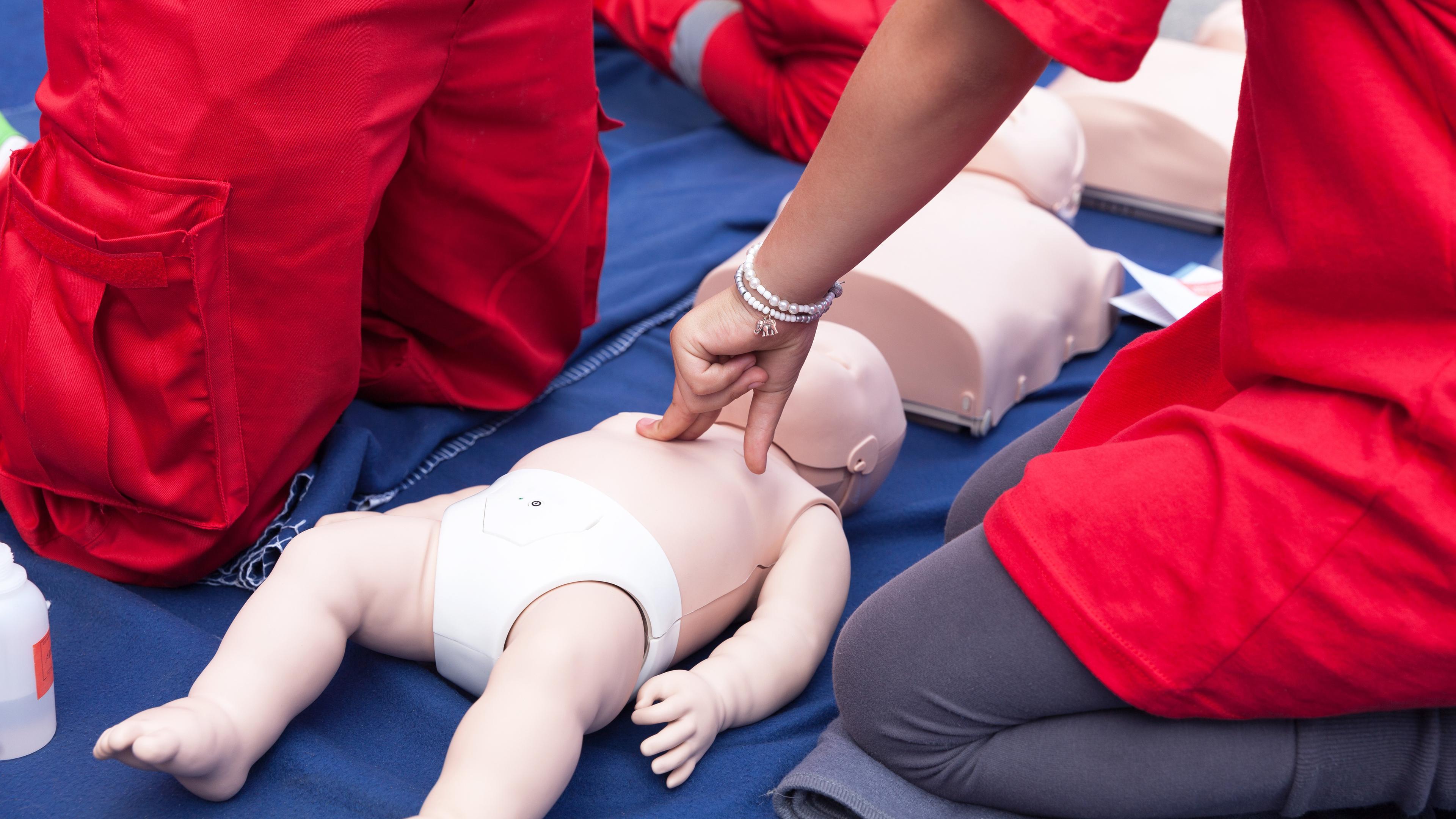 In einem Erste-Hilfe-Kurs wird an einer Puppe auf dem Boden liegend gezeigt, wie man ein Baby durch Herzdruckmassage wiederbelebt.