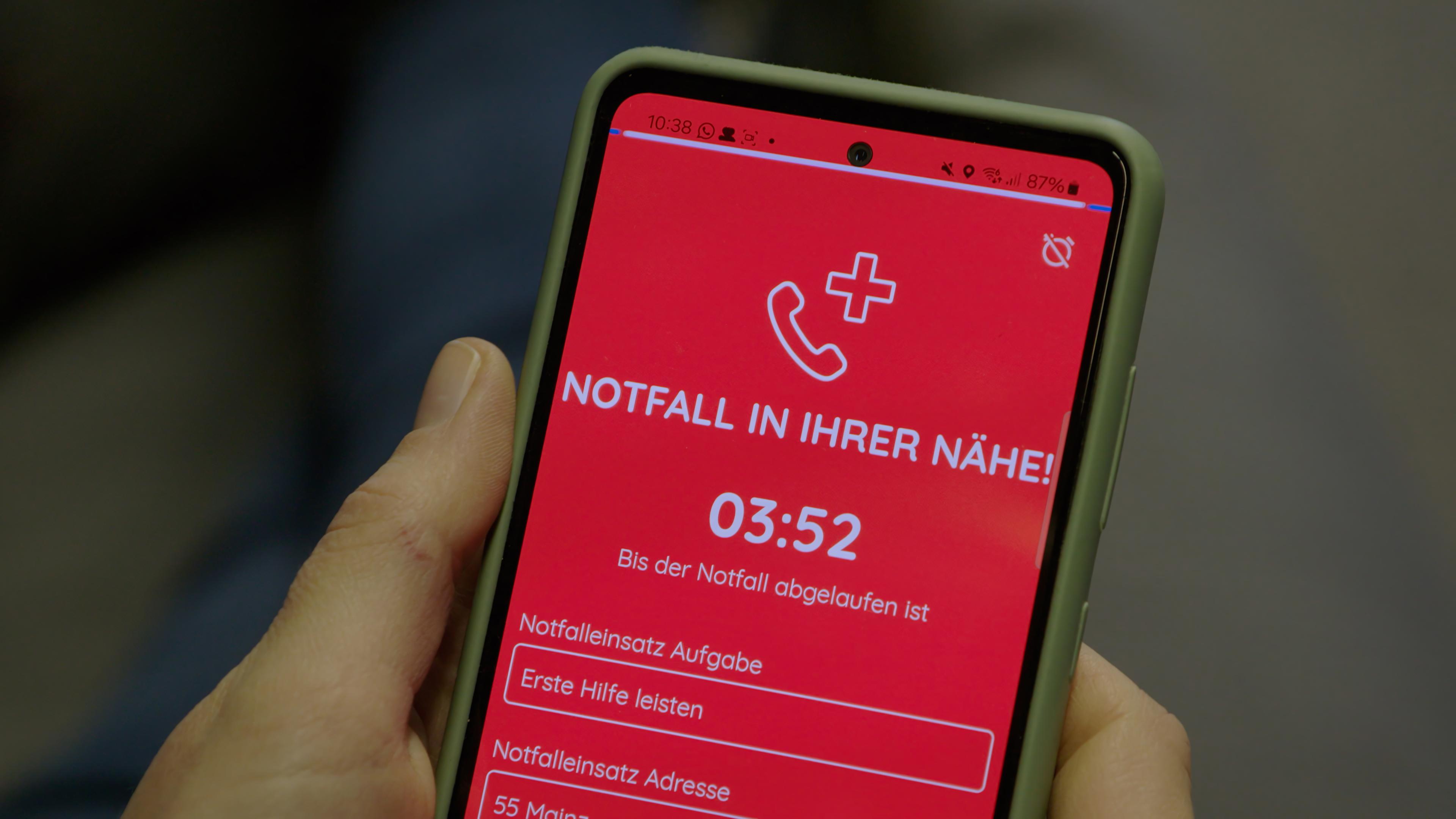 Ein Smartphone wird in der Hand gehalten, auf dem eine Ersthelfer-App einen aktuellen Notfall meldet.