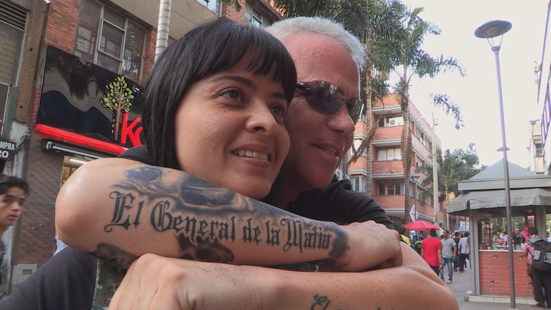 "Escobars Vollstrecker – Geständnisse eines Killers": Jhon Jairo Velásquez alias "Popeye" mit Sonnenbrille posiert mit einer Anhängerin in den Straßen Medellíns und umarmt sie von hinten.