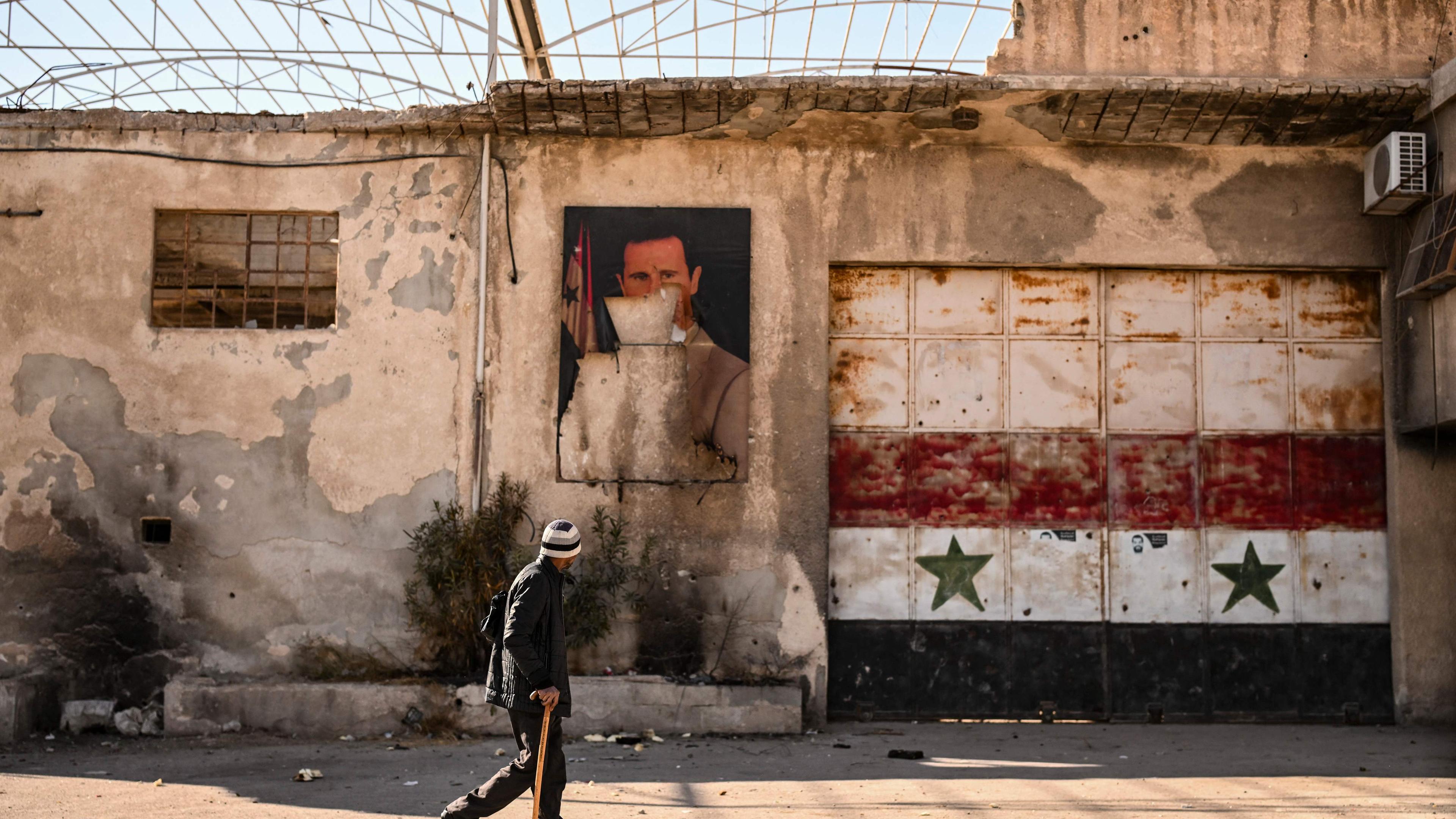 Ein Mann läuft an einem Portrait von dem gestürzten ashar al-Assad in der Stadt Adra vorbei.