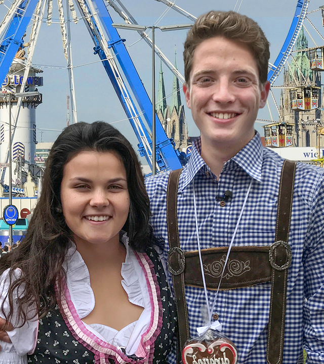 Louisa und Philip posieren in bayerischer Lederkluft vor einem Riesenrad.