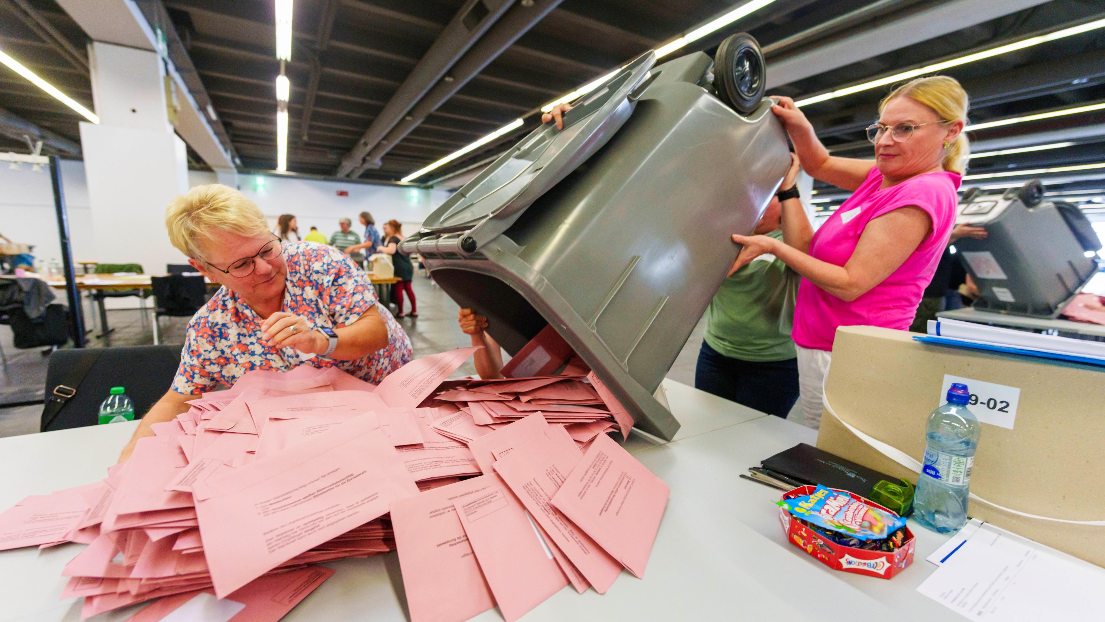 In Frankfurt am Main öffnen zwei Wahlhelferinnen um genau 15 Uhr die erste Briefwahlurne, auf einem Tisch liegen viele rosafarbene Umschläge mit Briefwahlstimmen.