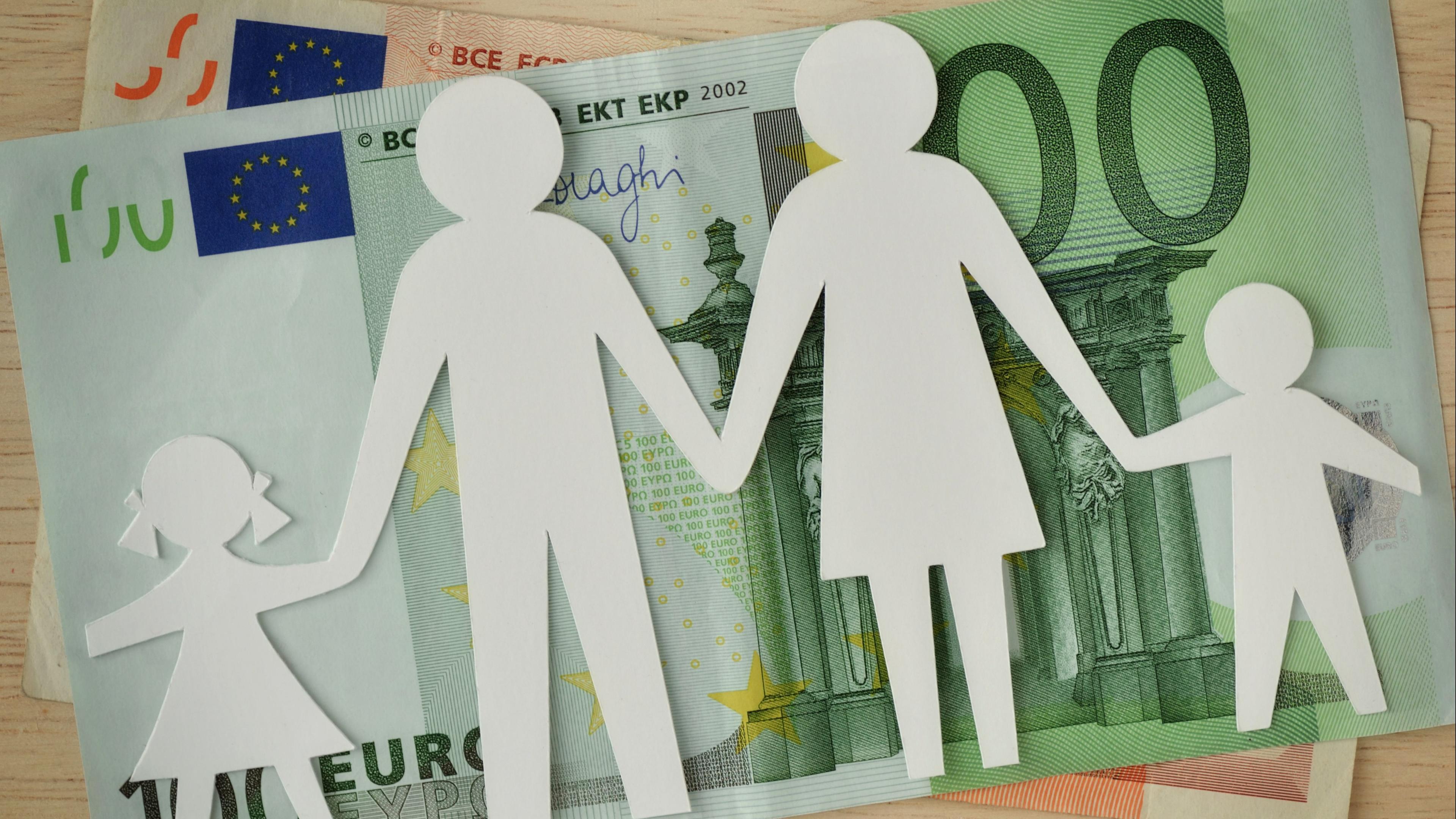 Eine Familie im Scherenschnitt liegt über einem 100-Euro-Schein.