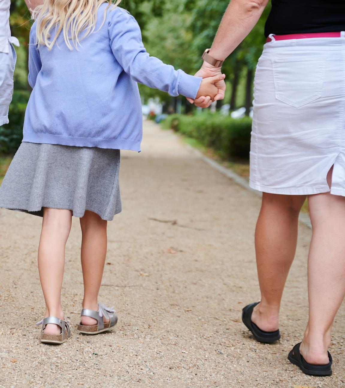 Ein Vater und eine Mutter halten die Hände ihrer Tochter, während sie auf einem Gehweg gehen. 