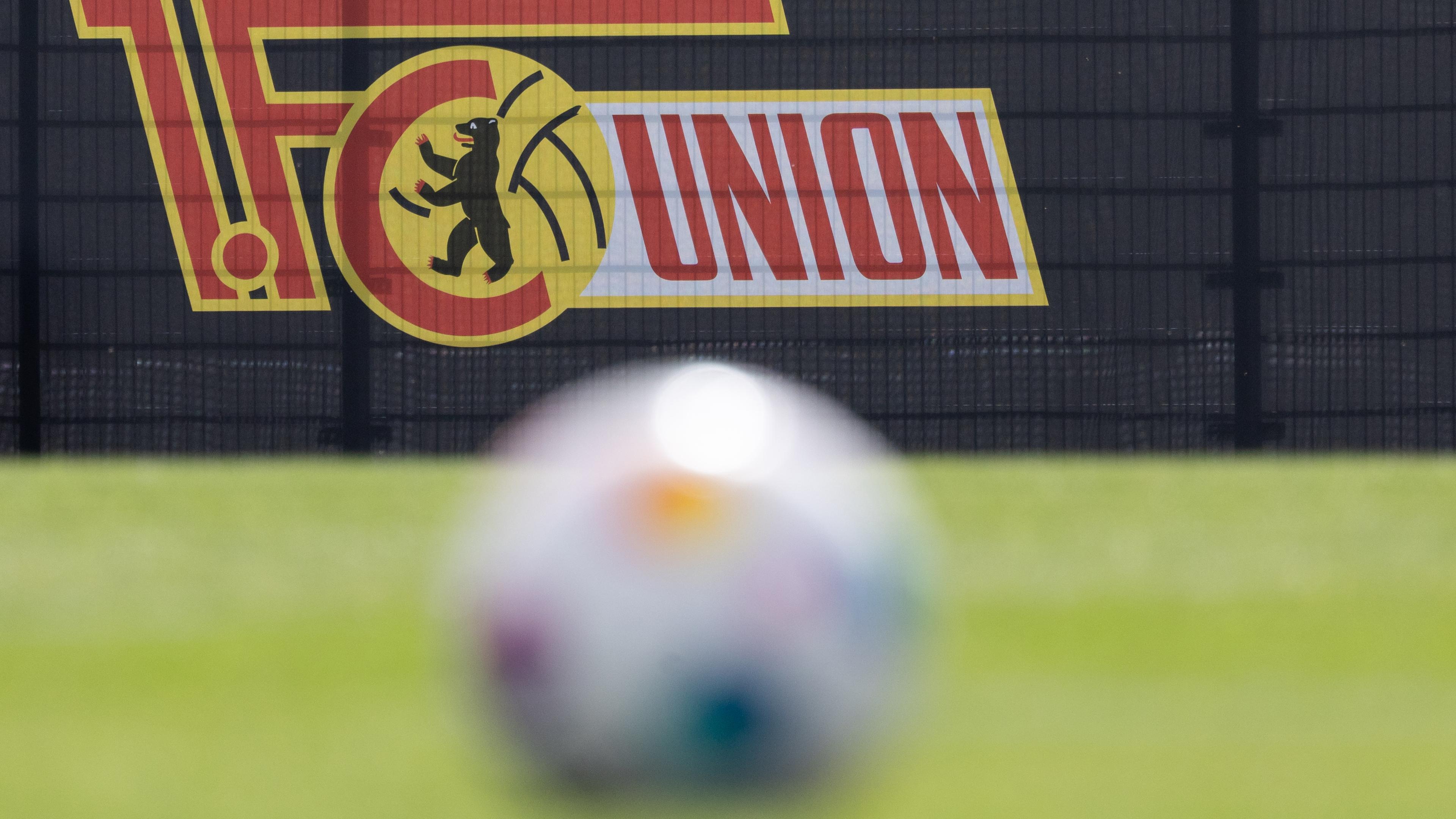 Ein Fußball liegt auf dem Rasen. Im Hintergrund ist das Logo vom 1. FC Eisern Union zu sehen.