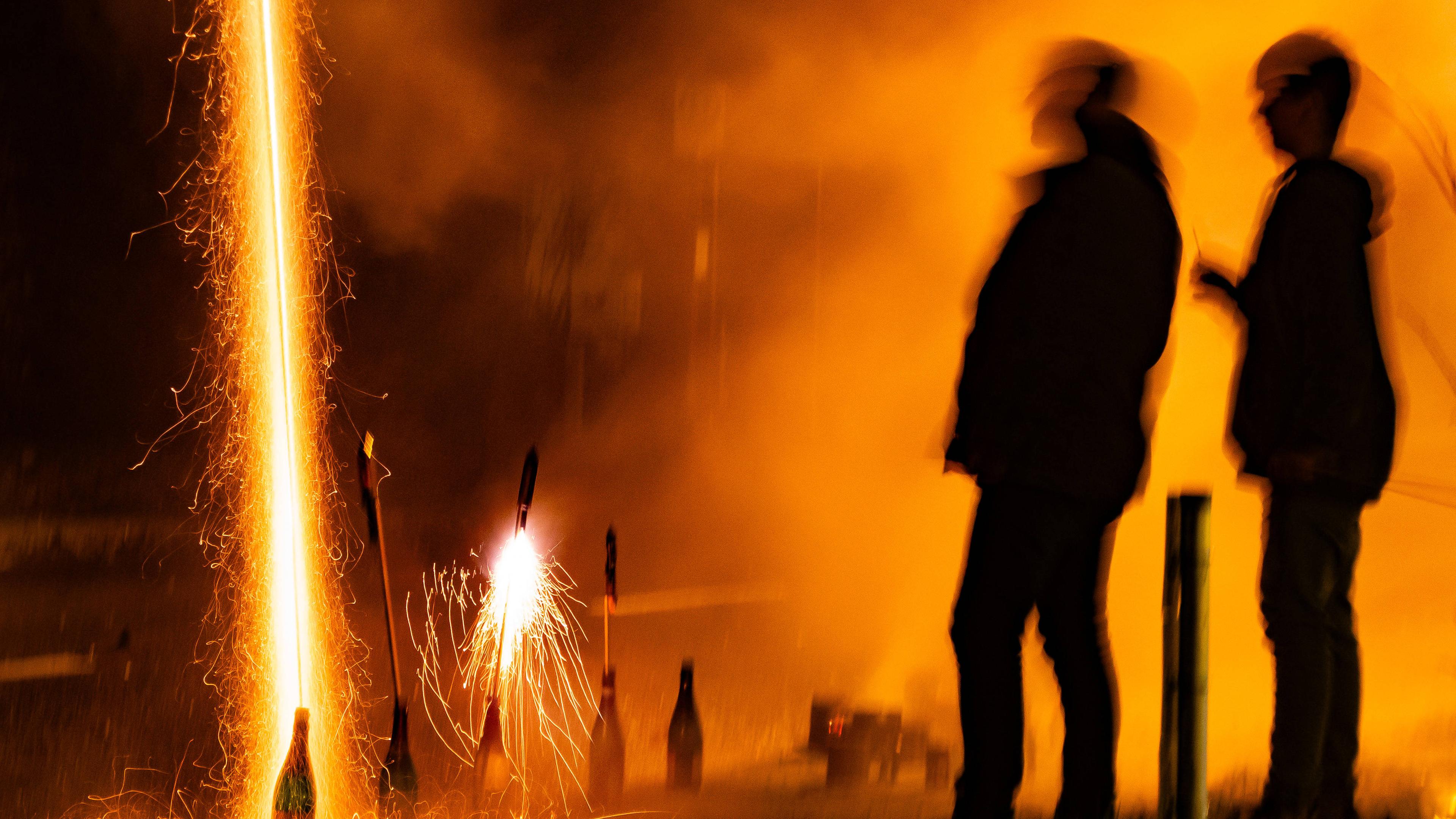 Zwei Männer zünden ein Feuerwerk aus Sektflaschen zu Silvester auf der Straße. 