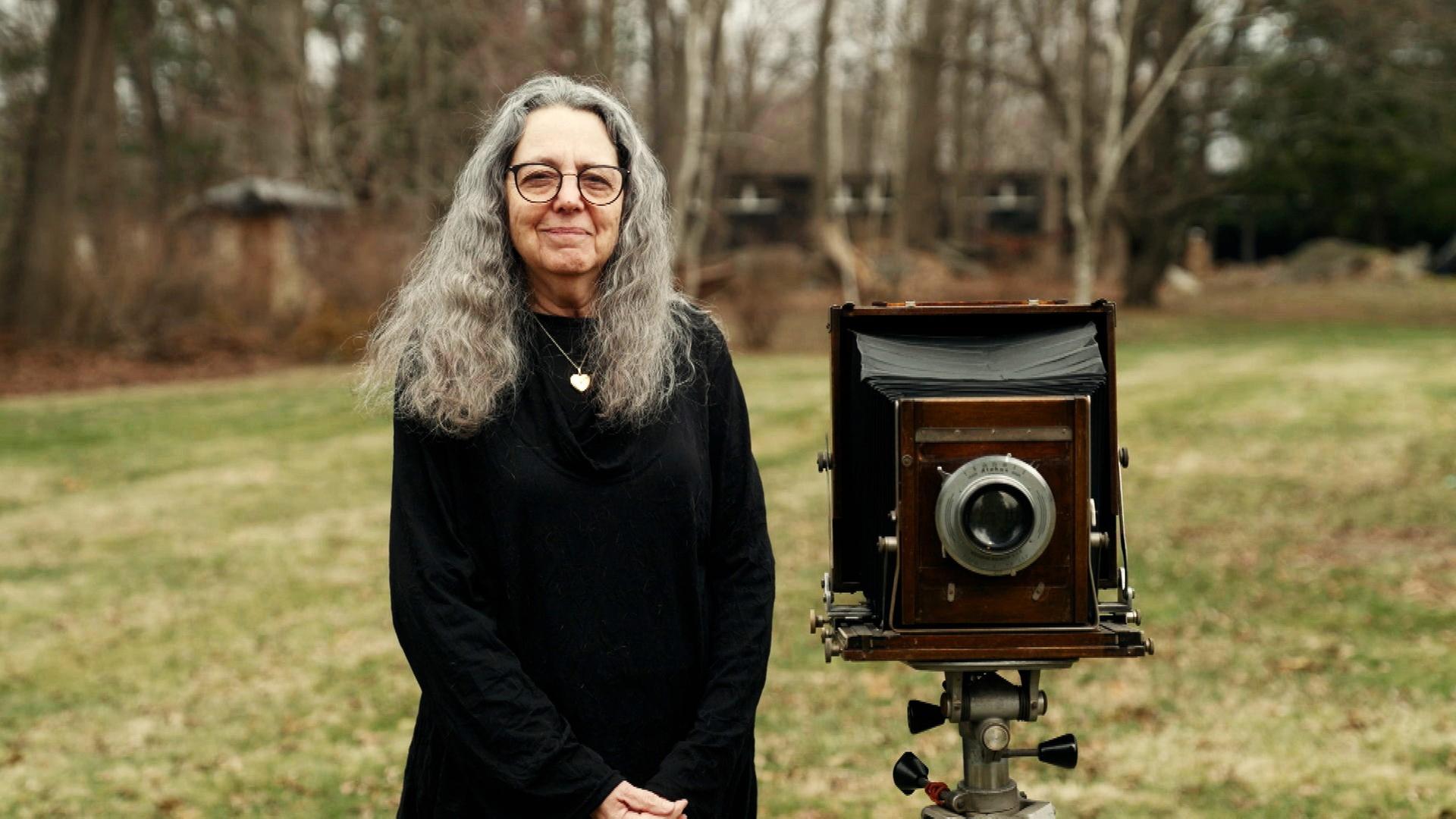Jill Enfield steht auf einer Wiese mit einer historischen Platten-Kamera.