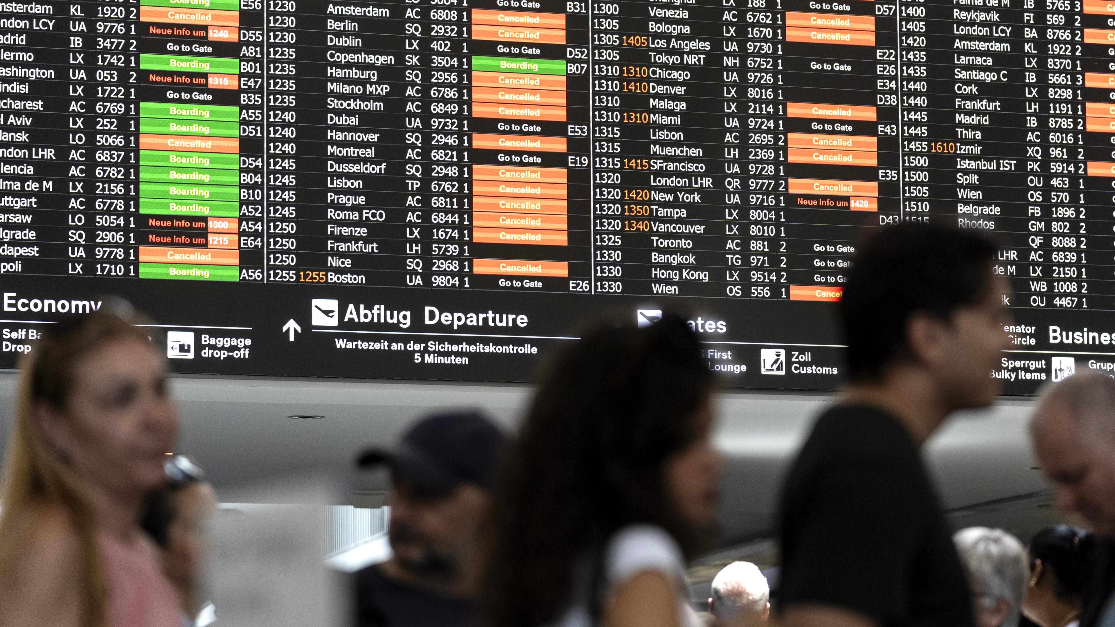 Reisende am Flughafen laufen vor einer Anzeigetafel her. Viele Flüge fallen aus.