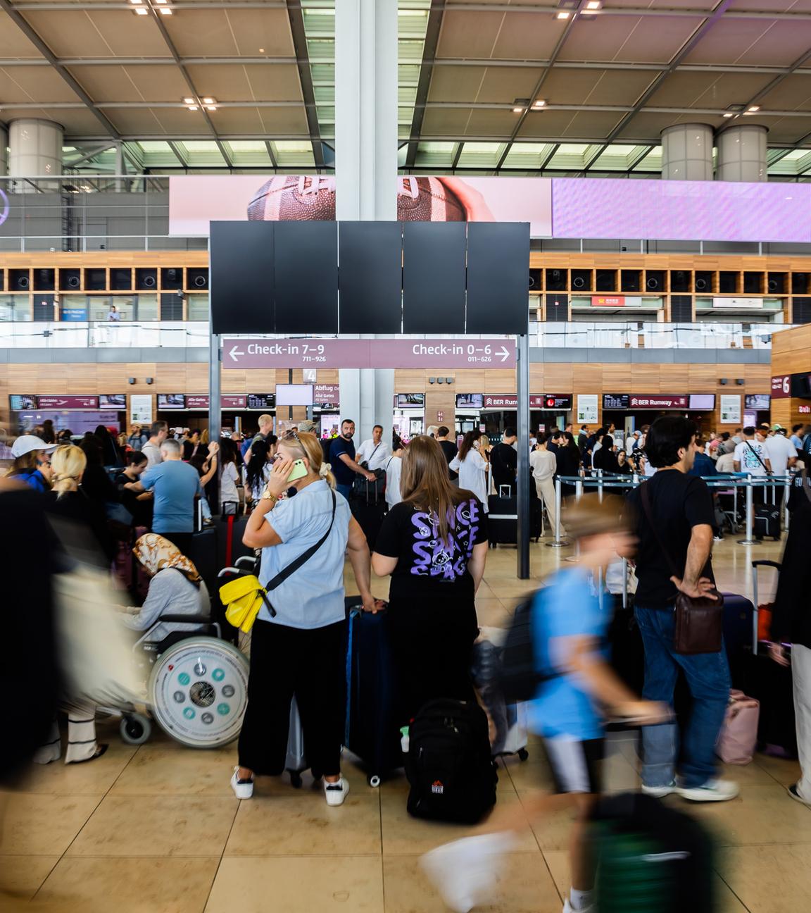  Zahlreiche Fluggäste warten am Hauptstadtflughafen BER vor einer schwarzen Anzeigetafel.