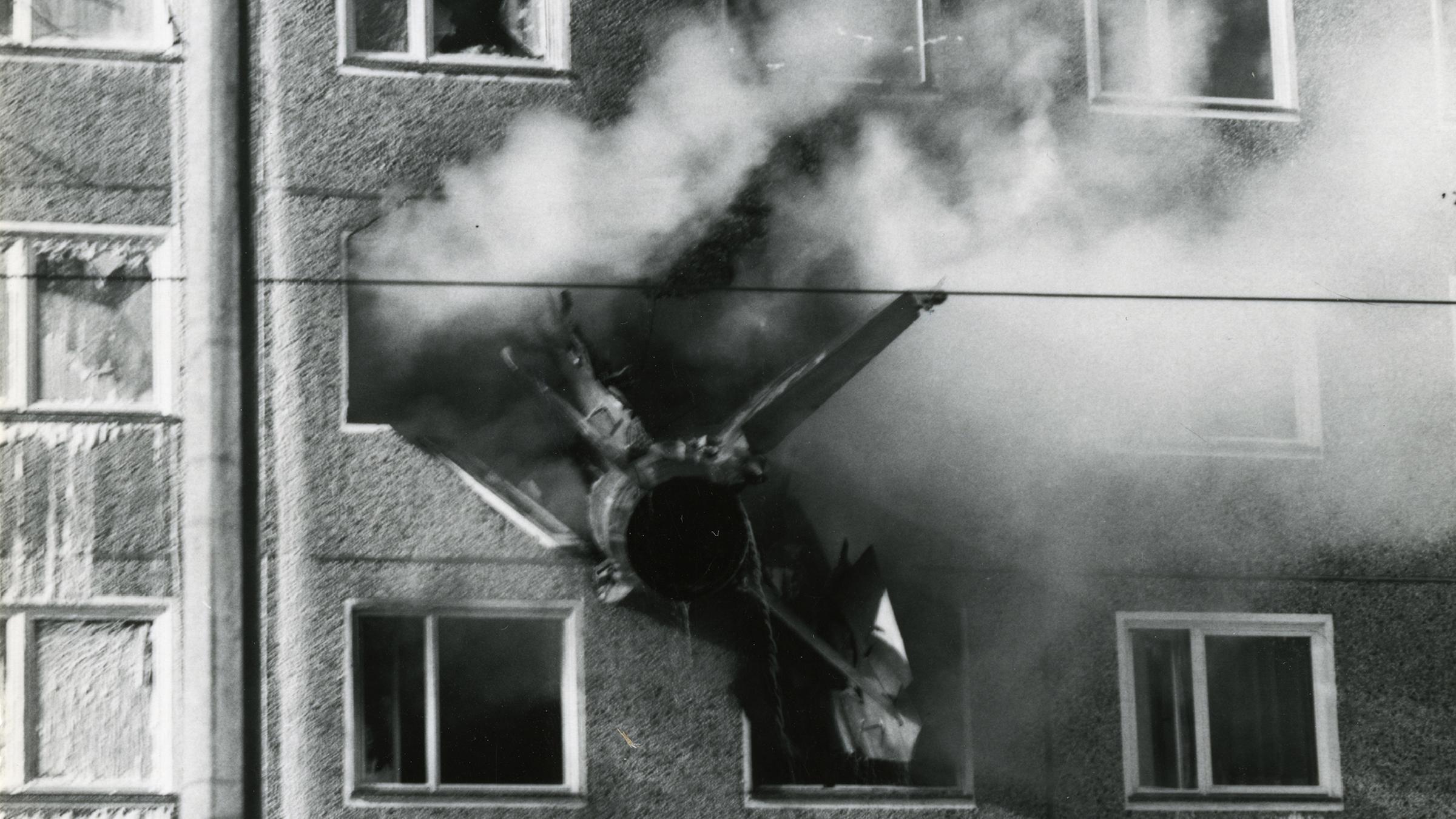 Das Wrack eines NVA-Kampfjets steckt in einer qualmenden Hausfassade.