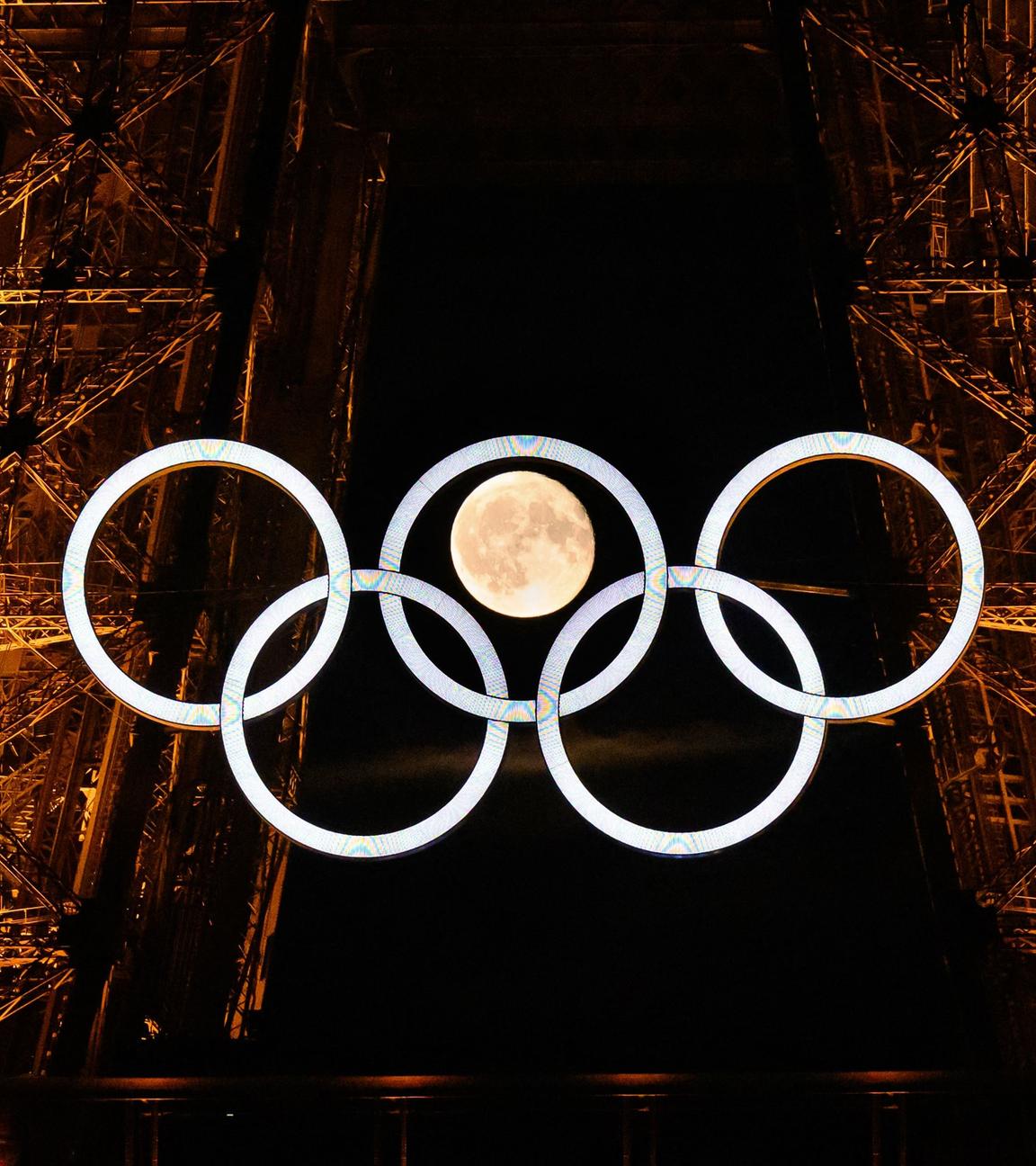 Die Olympischen Ringe am Eiffelturm mit dem Mond im Hintergrund