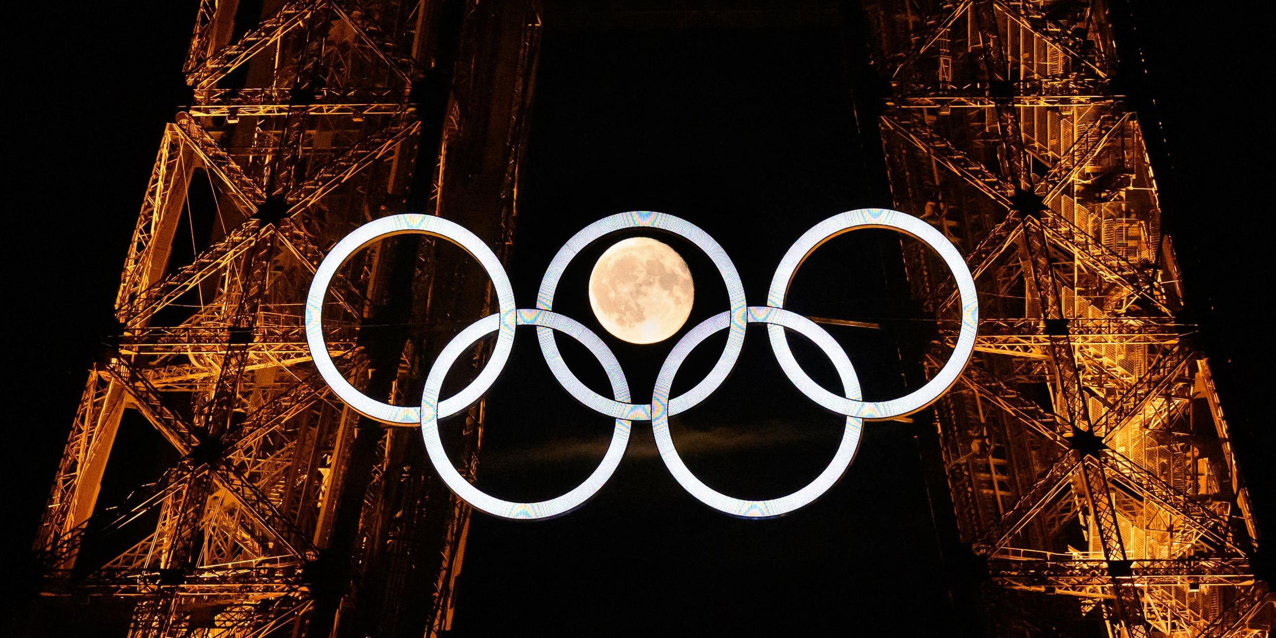 Die Olympischen Ringe am Eiffelturm mit dem Mond im Hintergrund