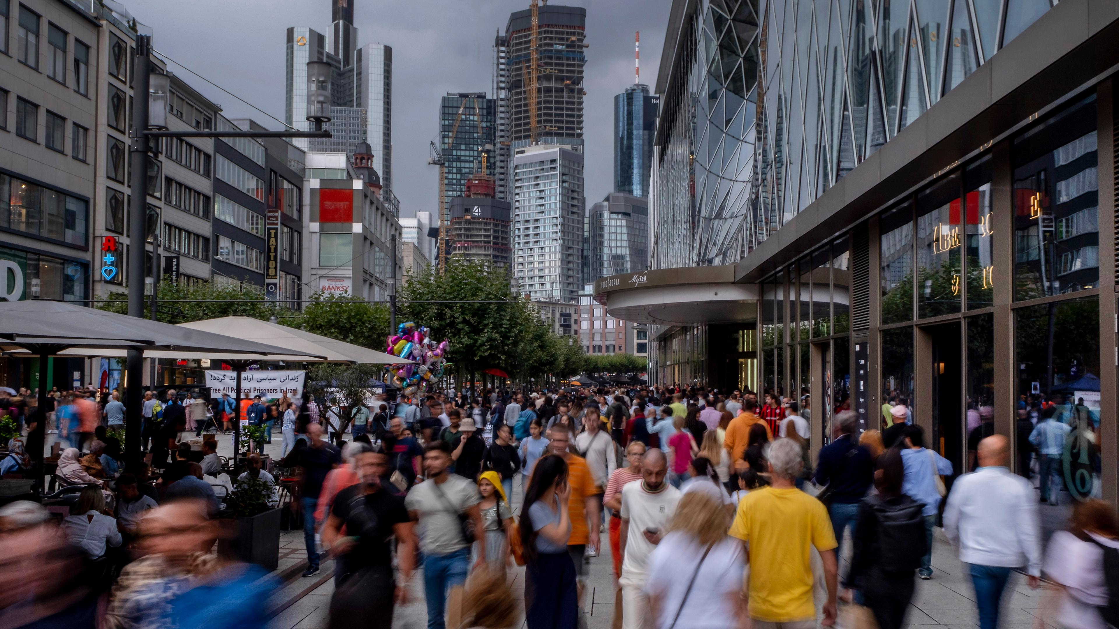 Man sieht Menschen auf der Zeil in Frankfurt am Main und Wolkenkratzer im Hintergrund.