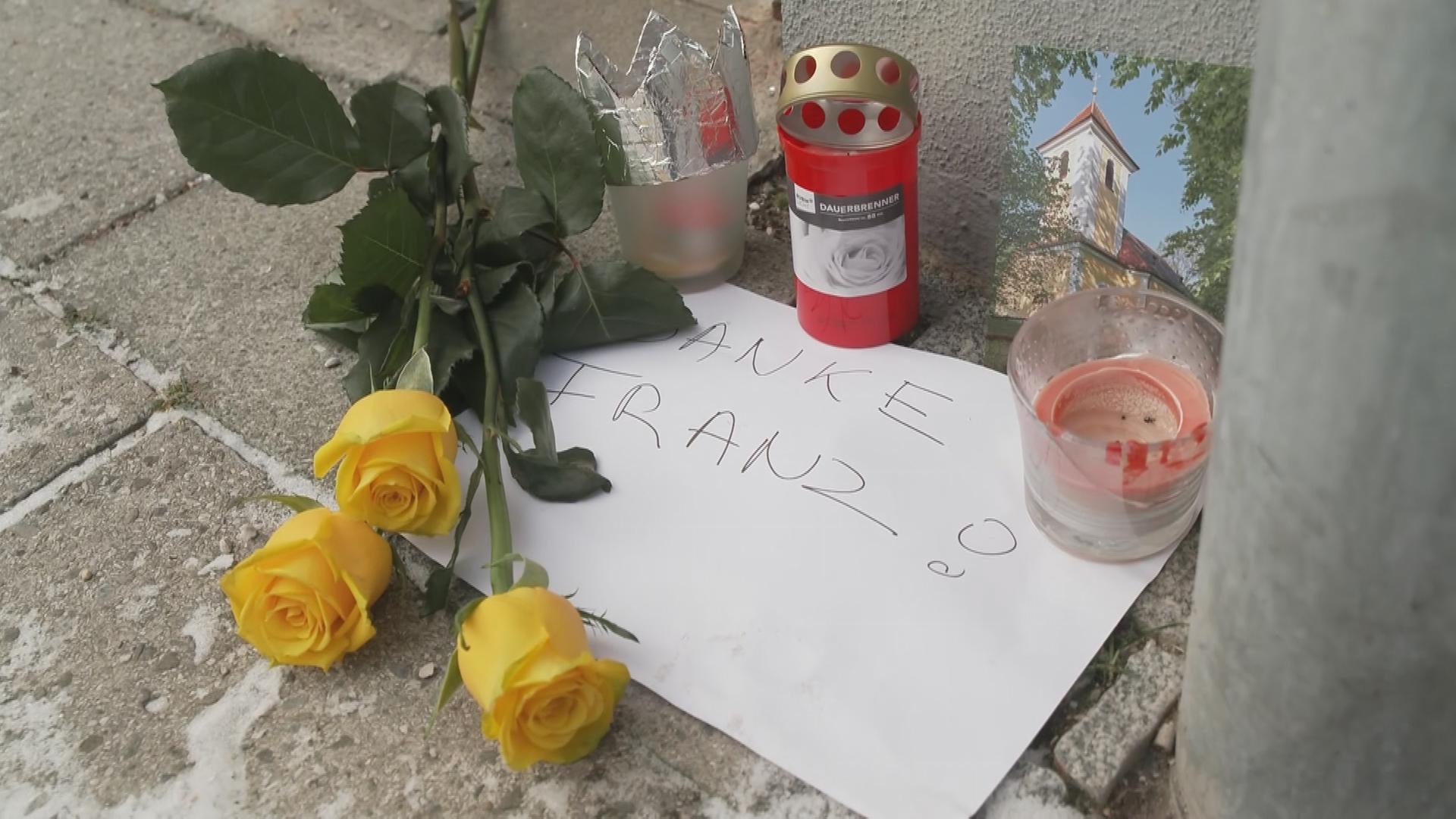 Trauerkerze und Blumen liegen auf einem Schild auf dem "Danke Franz" steht