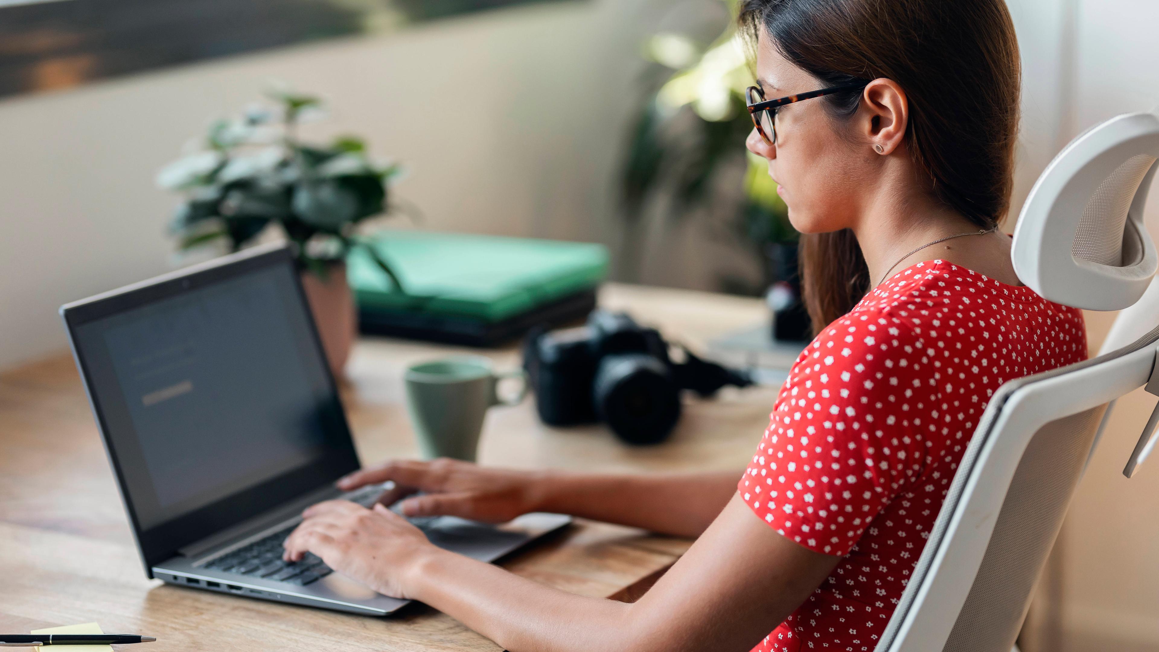 Eine Frau sitzt im Homeoffice an ihrem Schreibtisch und arbeitet mit einem Laptop.