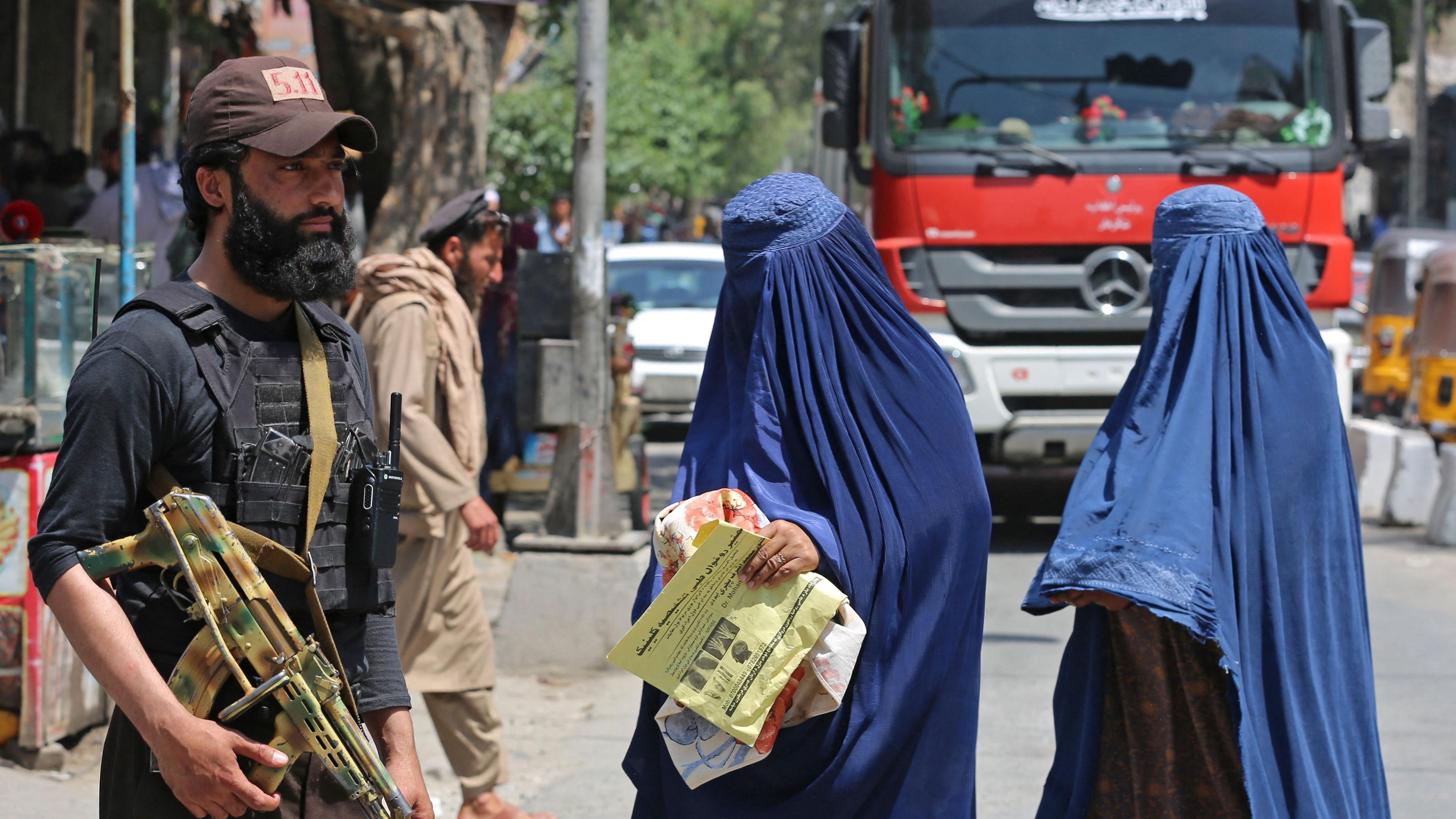 Afghanische Frauen in Burka neben einem Taliban-Anhänger