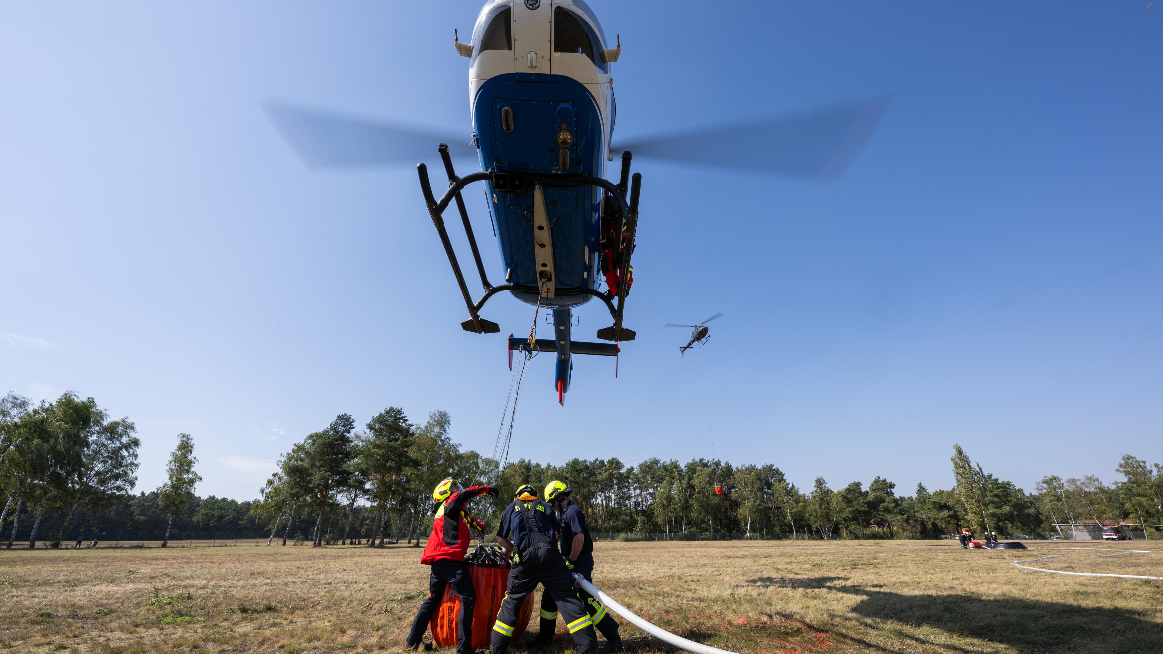 Niedersachsen, Bleckede: Freiwillige Feuerwehrleute bekommen bei einer Übung zur Waldbrandbekämpfung eine Unterweisung zum Befüllen eines Löschwasserbehälters, dem sogenannten Bambi Bucket, an einem Hubschrauber der Polizei.