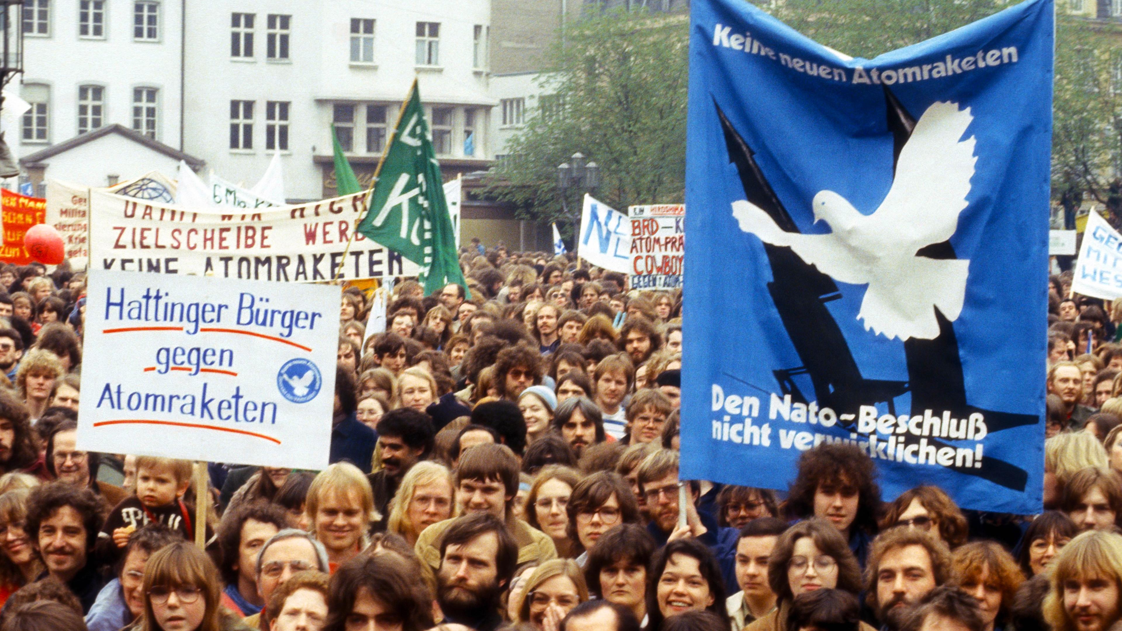 Eine große Menschenmenge demonstriert mit großen Plakaten, auf denen unter anderem eine Friedenstaube zu sehen ist.