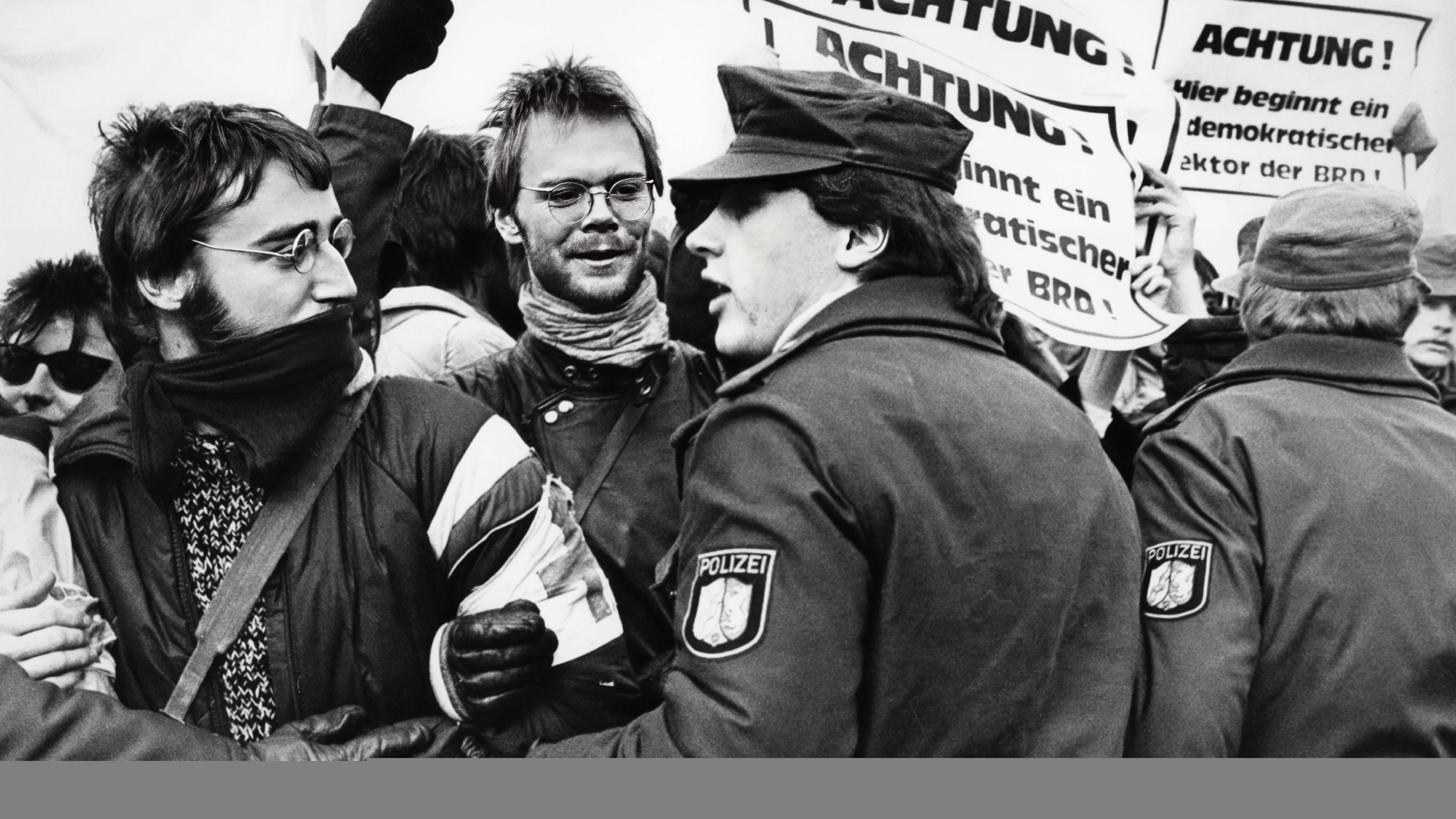 Polizisten drängen bei einer Demonstration Männer mit Plakaten zurück.