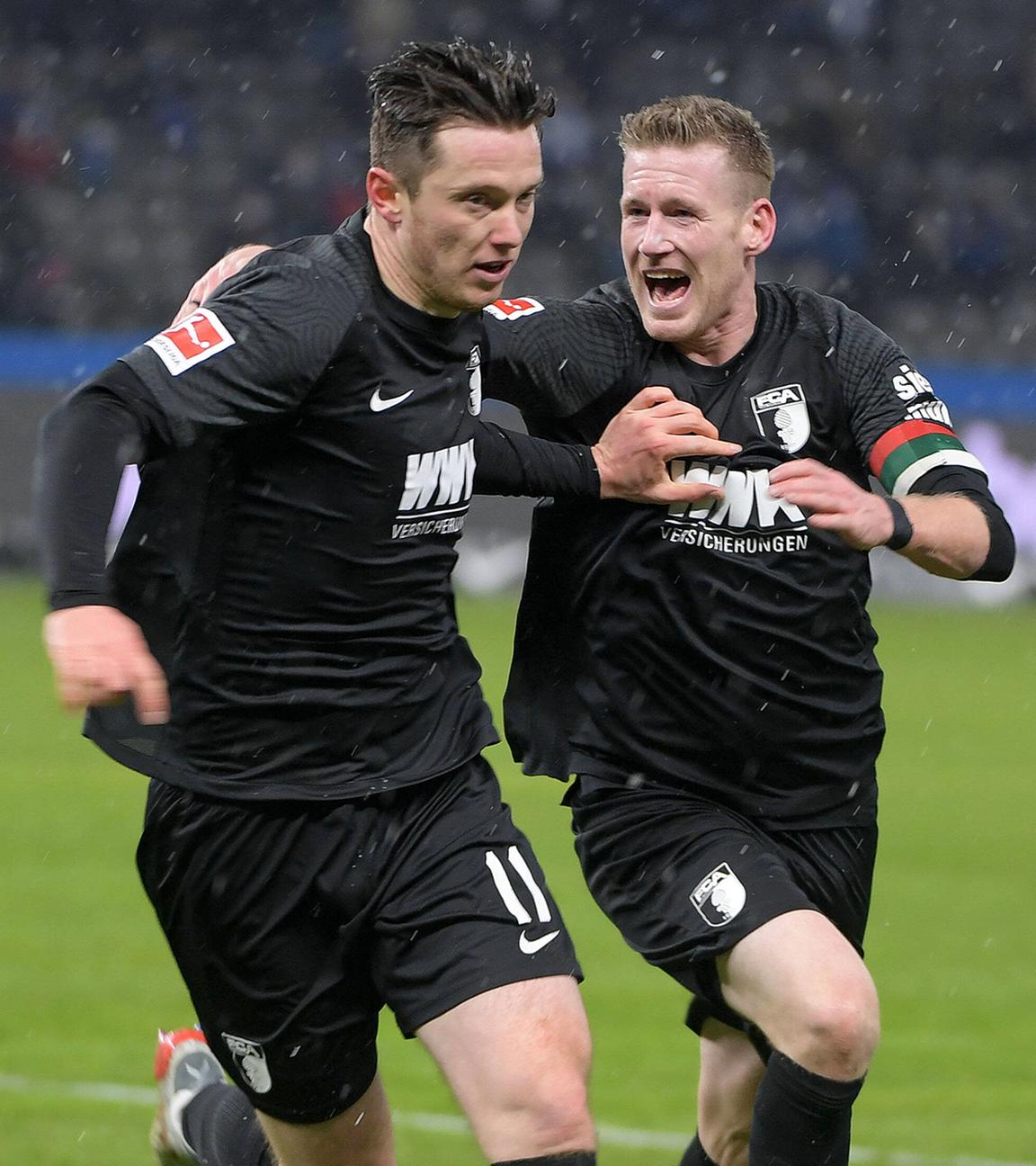 Augsburgs Andre Hahn (r) und Michael Gregoritsch (m) freuen sich über den Treffer zum 1:1 gegen Hertha BSC am 27.11.2021 in Berlin.