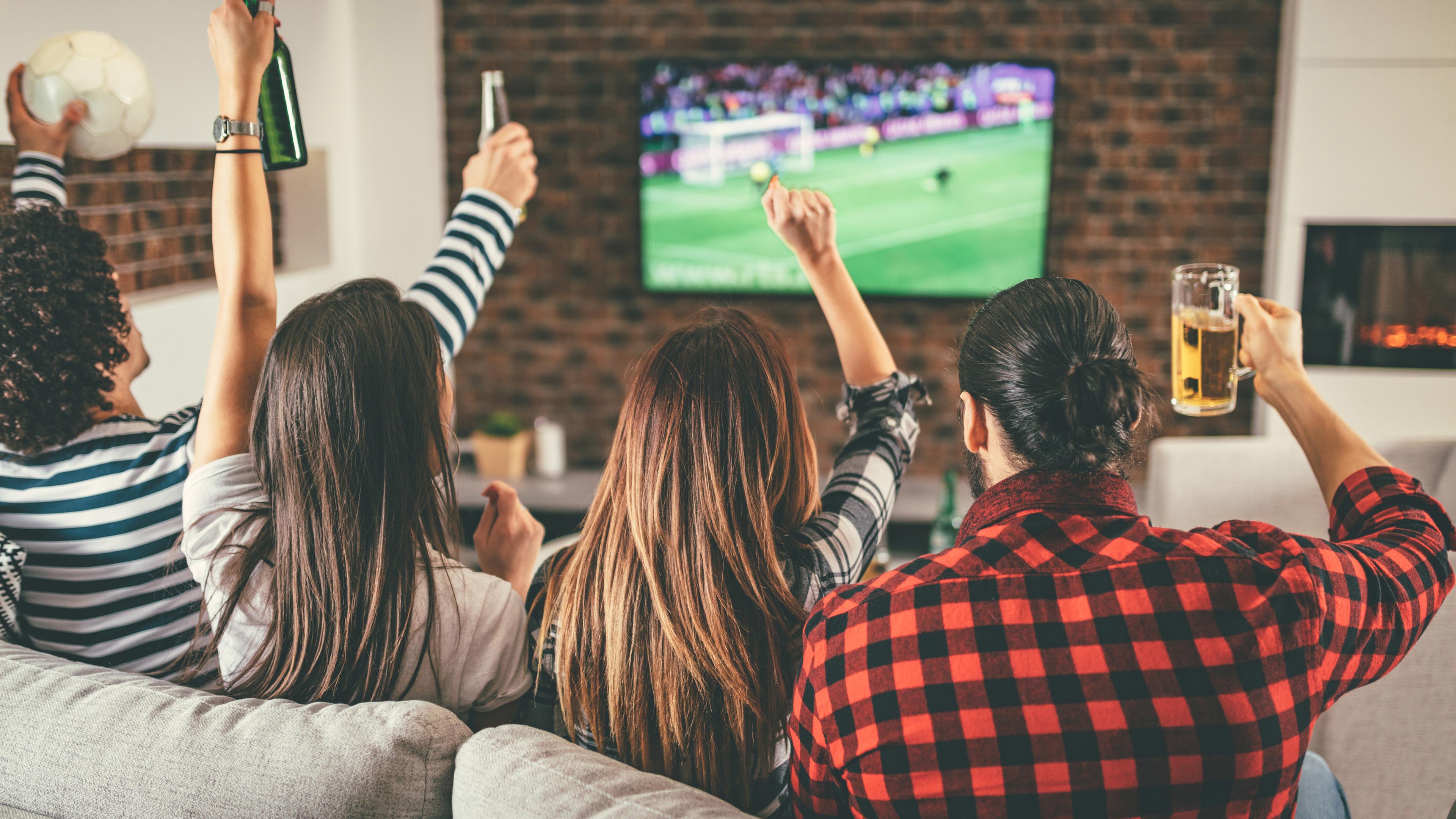 Freunde jubeln vor dem Fernseher beim Schauen eines Fußballspiels.