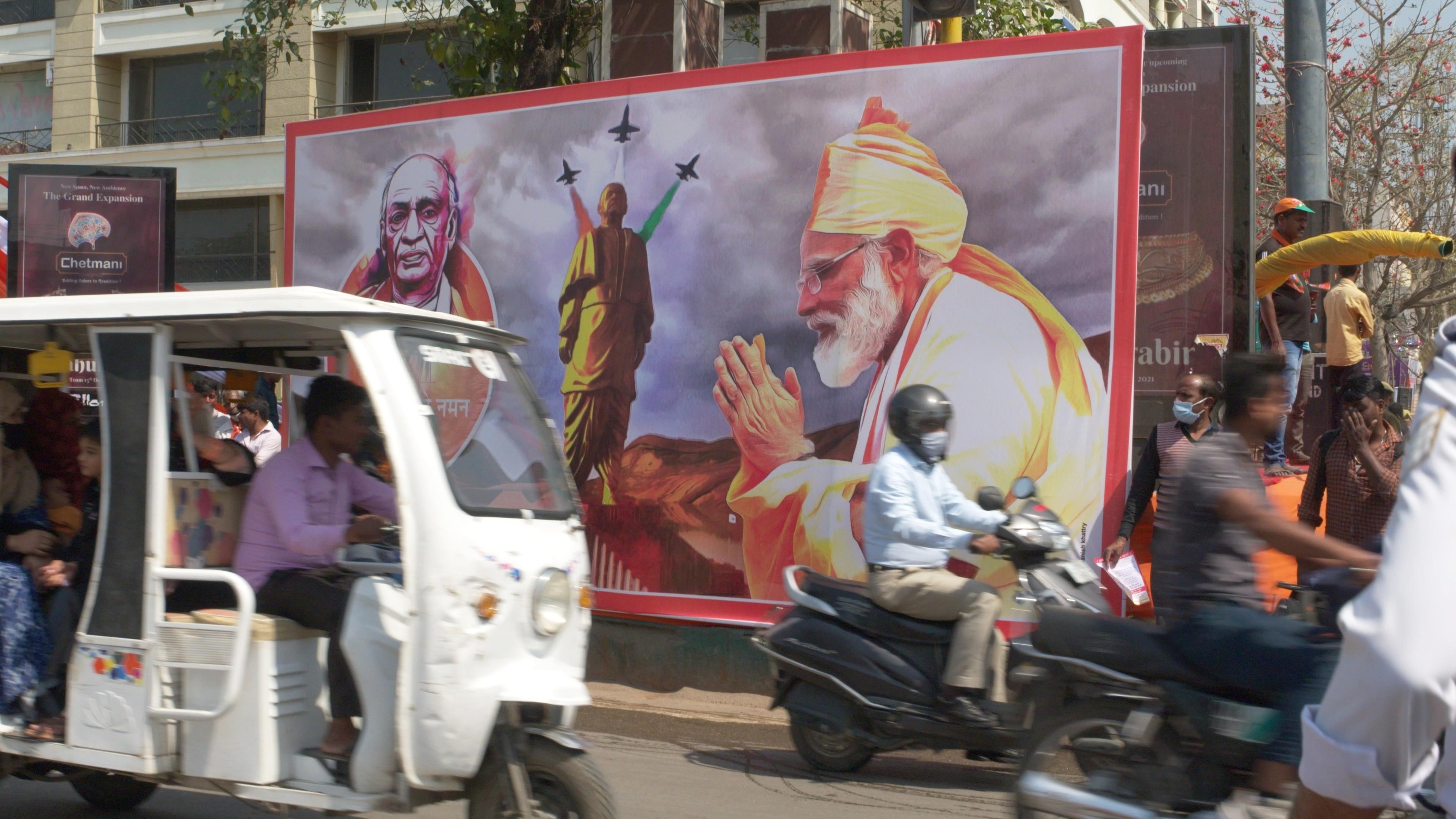  Straßenszene mit Mopeds, großes Wahlplakat der Regierungspartei BJP, auf dem Premierminister Narendra Modi zu sehen ist.