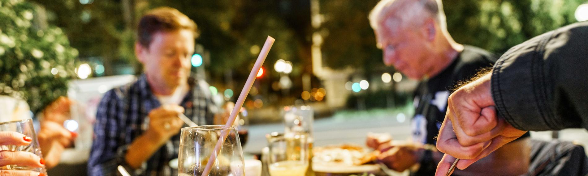 Menschen sitzen im Außenbereich eines Restaurants und essen u.a. Pizza.