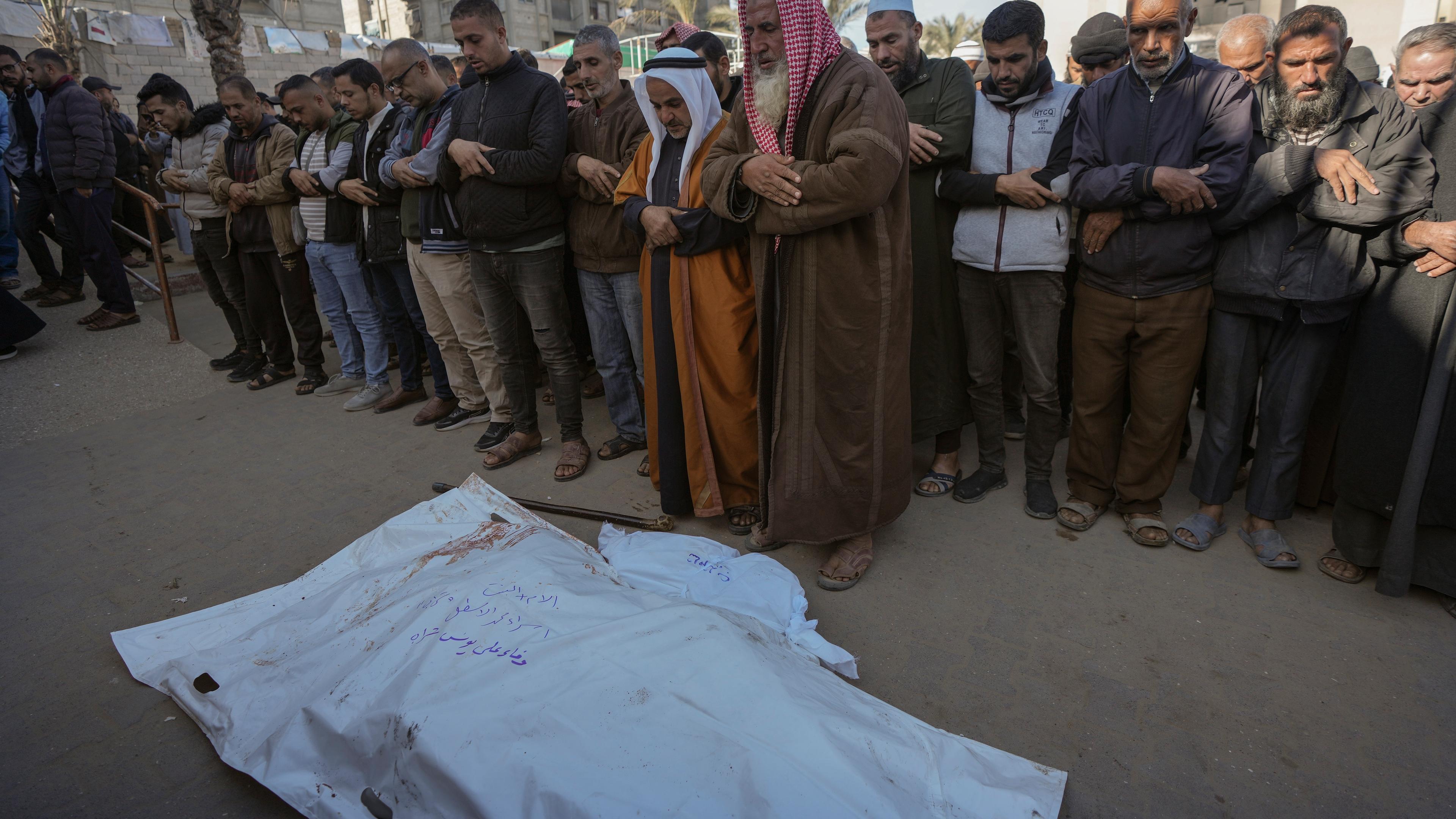 Men pray over the bodies of victims of an Israeli airstrike at the Muwassi camp