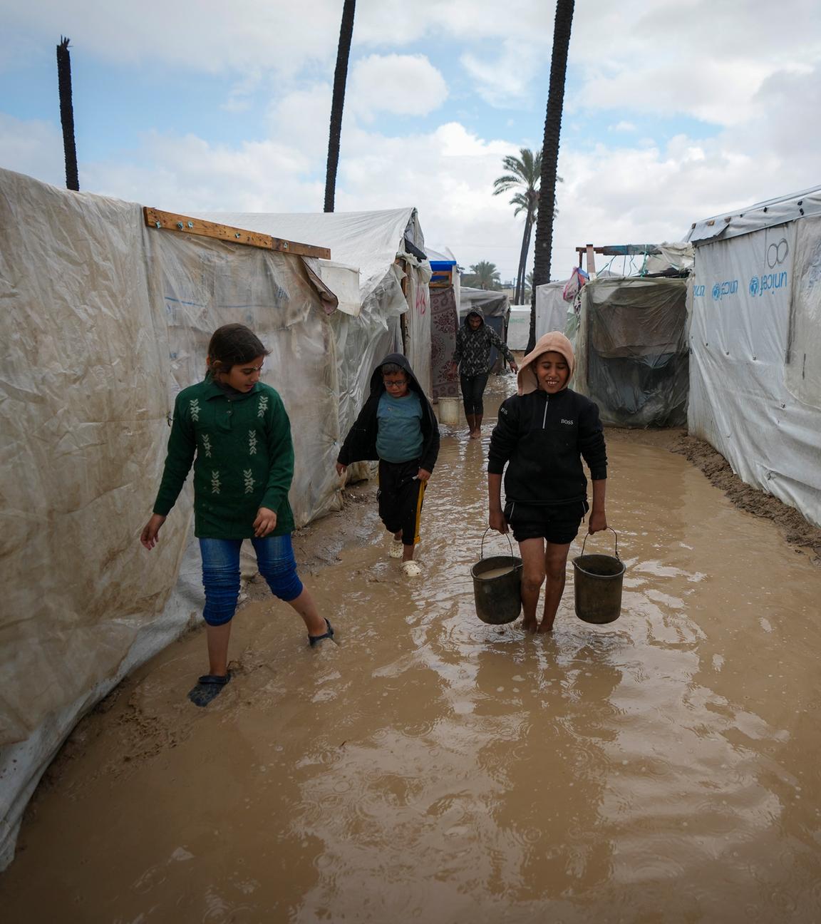 Palästinensische Kinder tragen Eimer mit Wasser nach nächtlichen Regenfällen im Flüchtlingszeltlager für vertriebene Palästinenser in Deir al-Balah im zentralen Gazastreifen