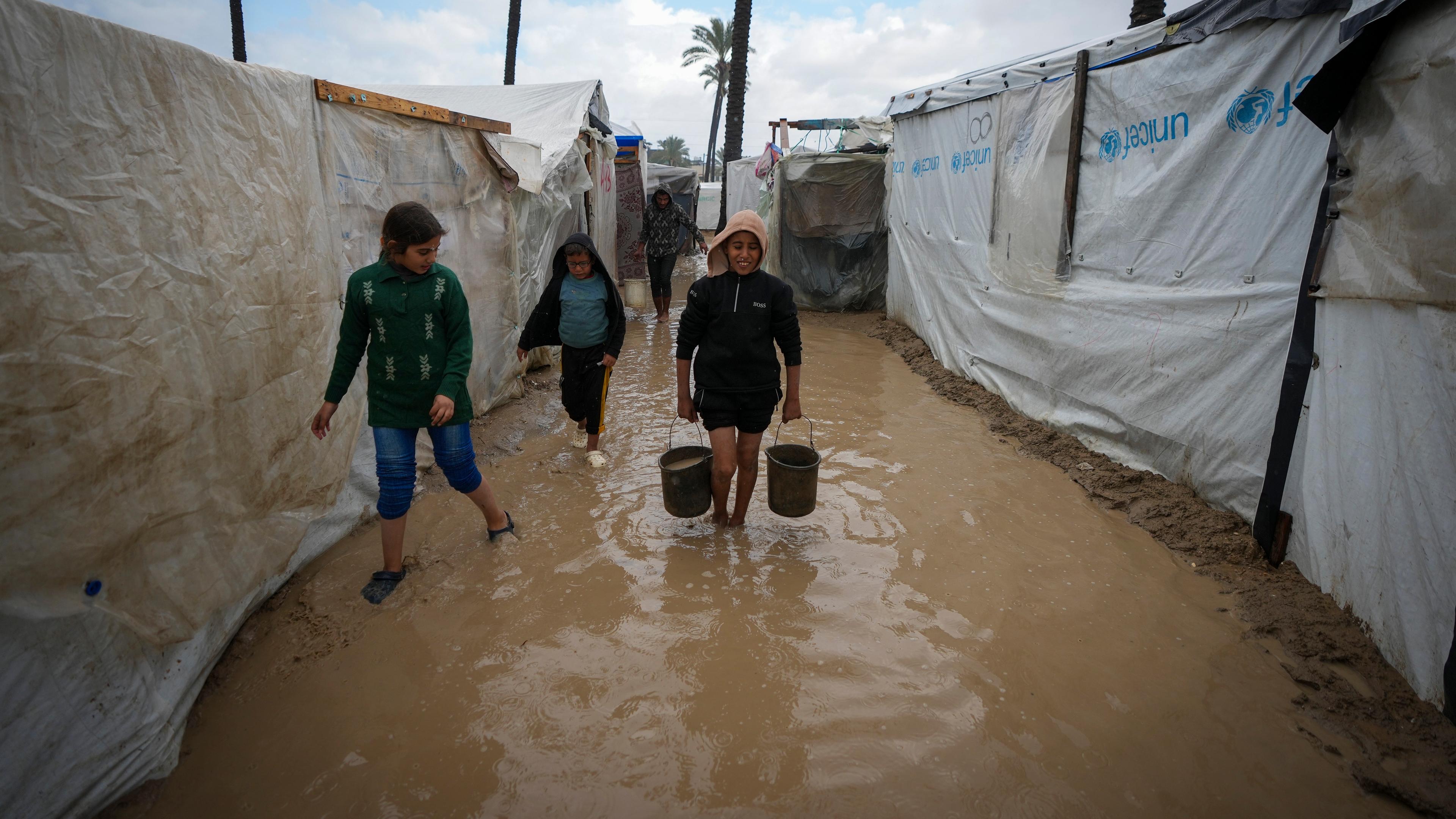 Palästinensische Kinder tragen Eimer mit Wasser nach nächtlichen Regenfällen im Flüchtlingszeltlager für vertriebene Palästinenser in Deir al-Balah im zentralen Gazastreifen