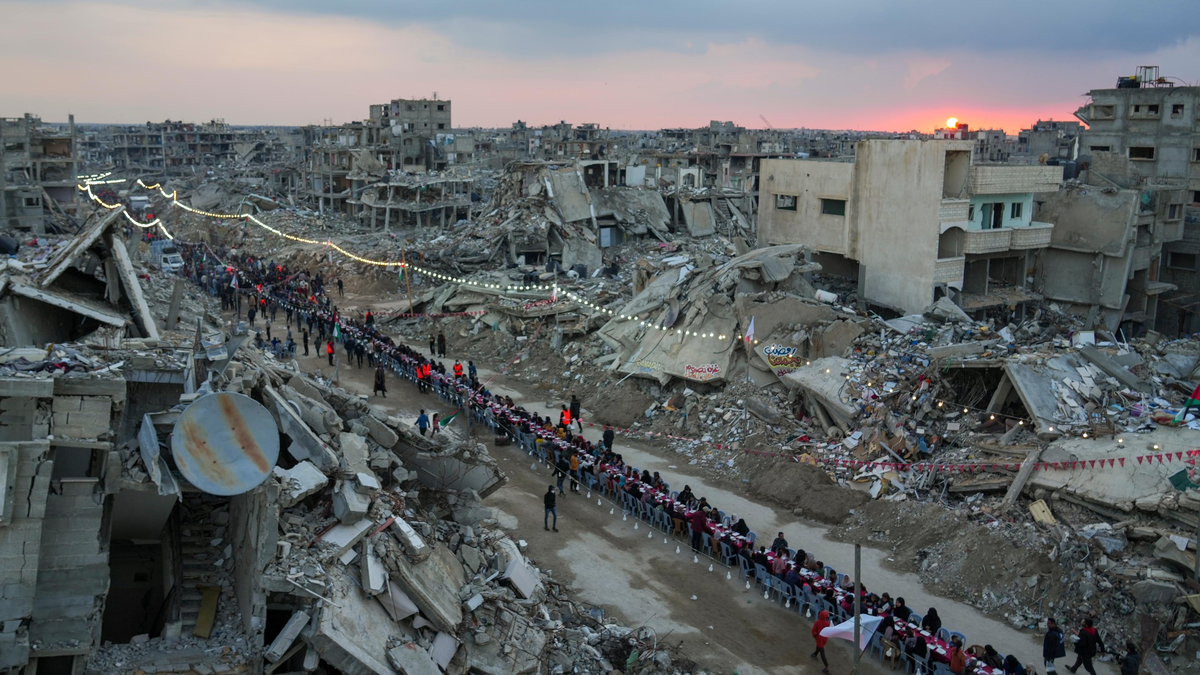 Bei Sonnenuntergang sitzen Palästinenser in Rafah an einem großen Tisch, umgeben von Trümmern zerstörter Gebäude. 