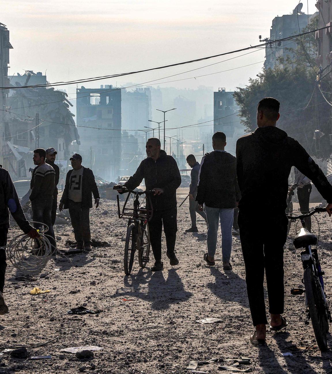 Männer gehen mit Fahrrädern durch Trümmer in in Gaza-Stadt.