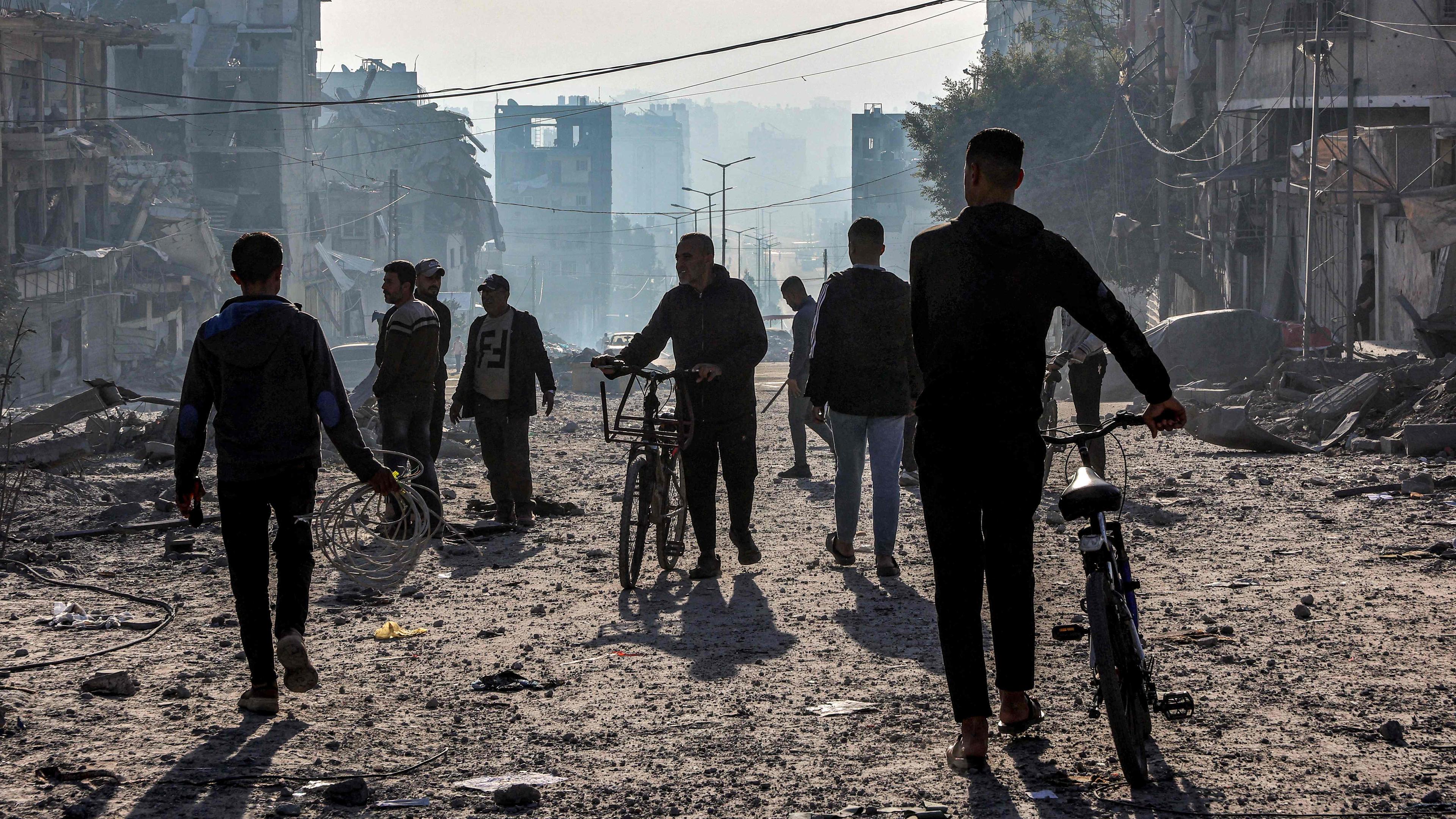 Männer gehen mit Fahrrädern durch Trümmer in in Gaza-Stadt.