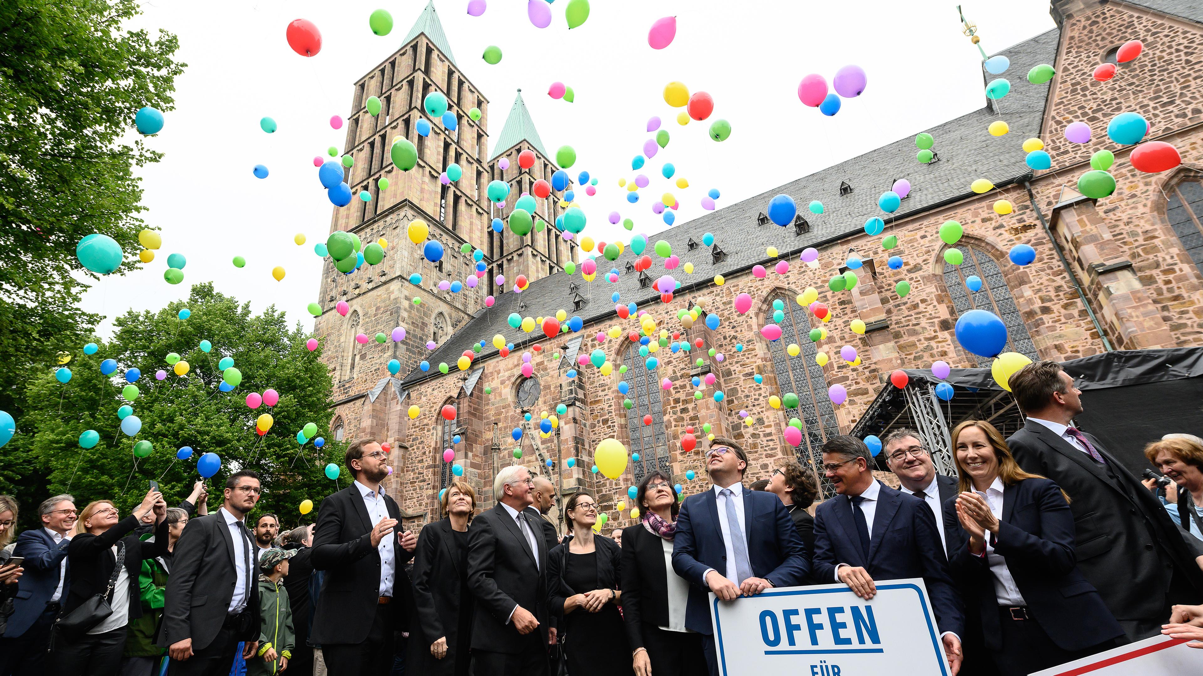 Steinmeier und weitere Gäste lassen vor einer Kirche in Kassel bunte Ballons fliegen.