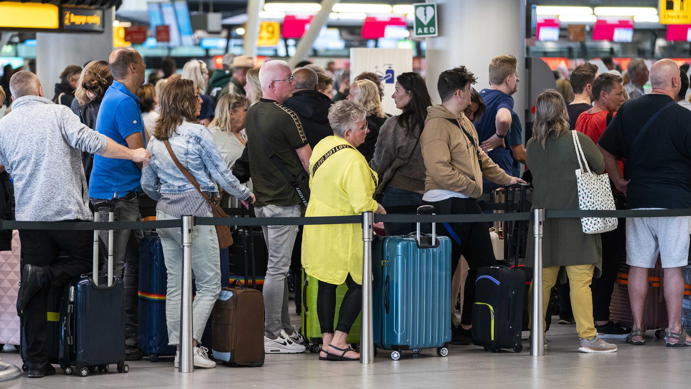 Reisende stehen in der Abflughalle des Flughafens Schiphol Schlange. 