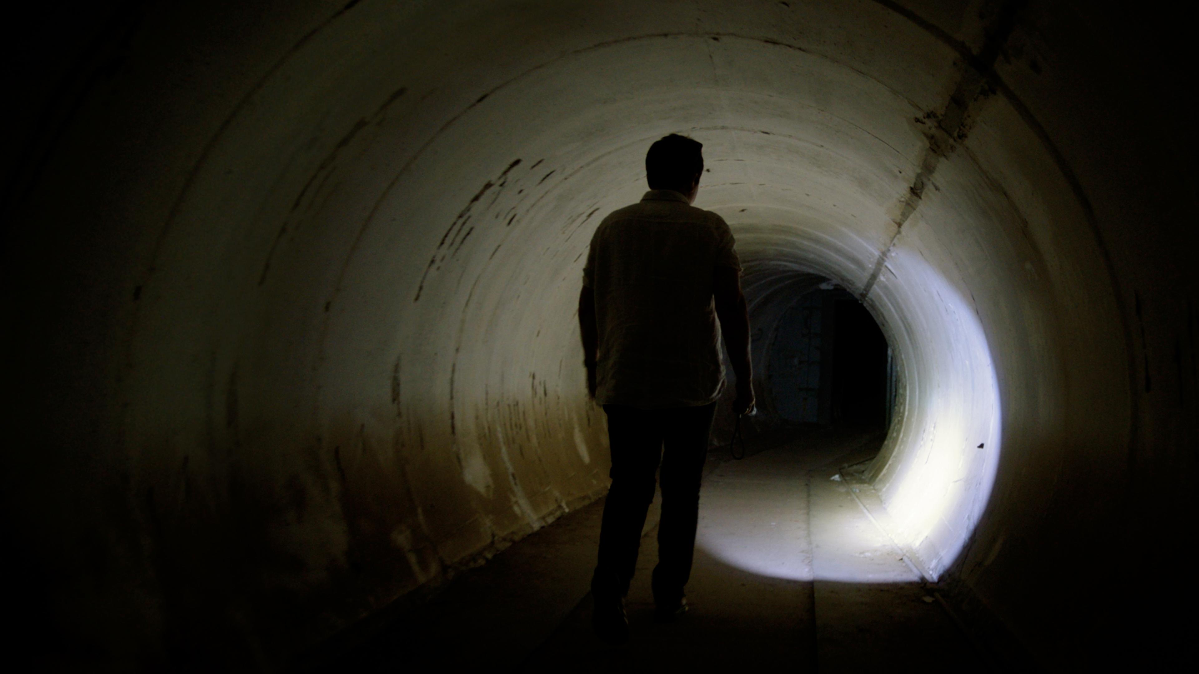 Bunkerexpertin Sylvia Rademacher steht in einem dunklen tunnelartigen Raum. Sie hält eine Taschenlampe in der Hand und leuchtet den Bereich vor sich aus.