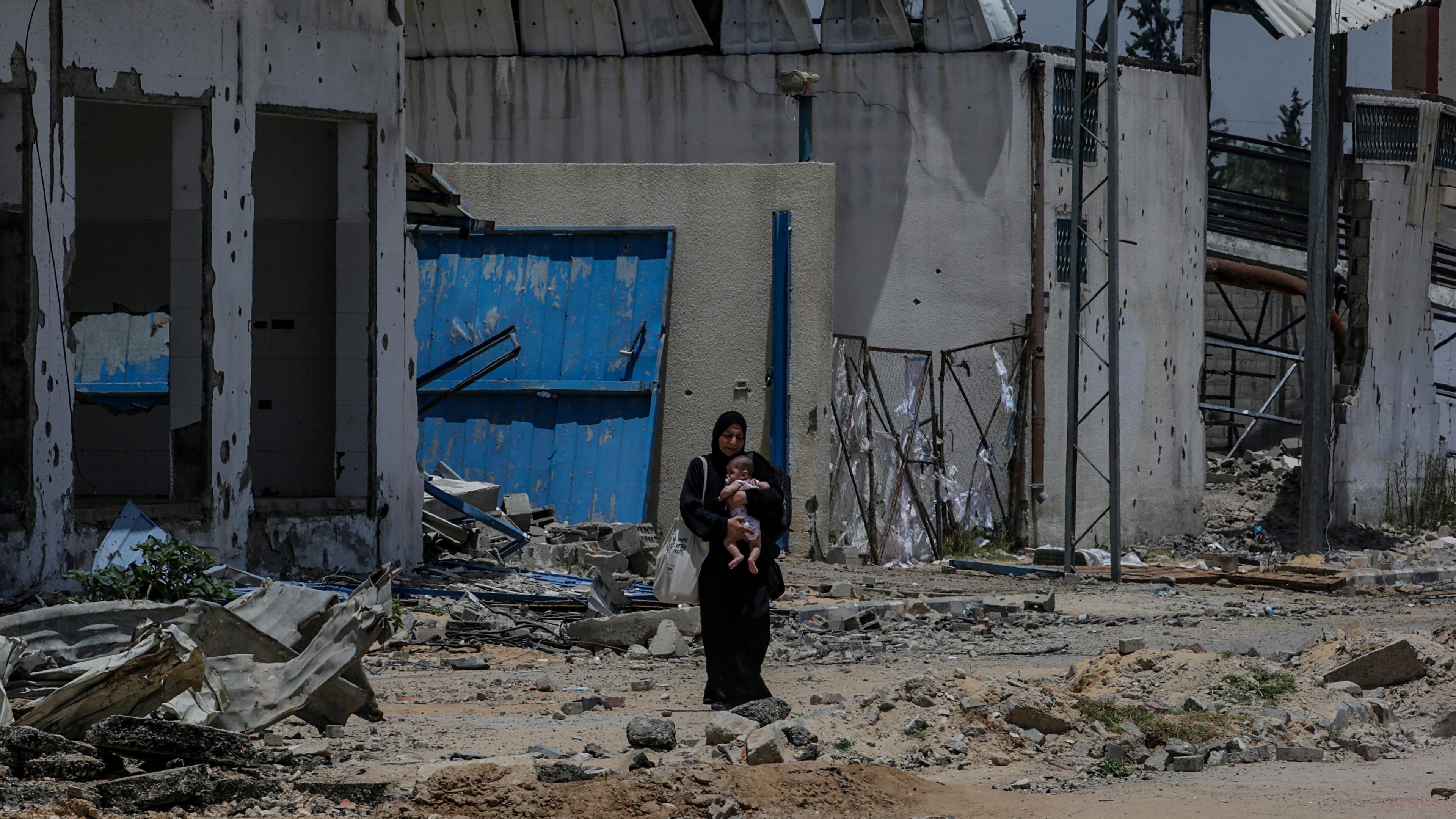 Eine Frau steht mit ihrem Kind vor zerstörten Gebäuden im Flüchtlingslager Nusairat aus dem heute Morgen vier israelische Geiseln befreit worden waren.