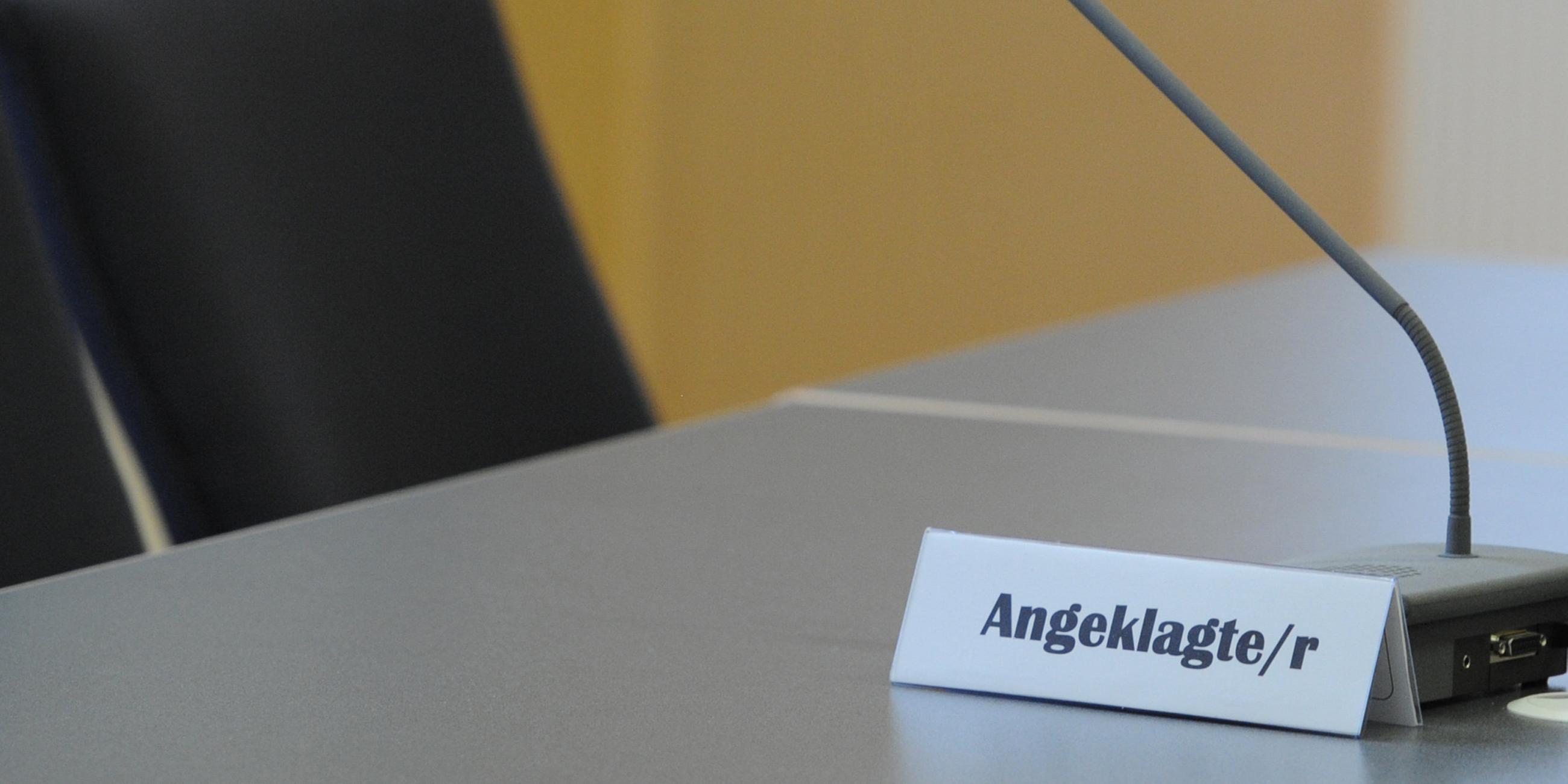 Der Sitzplatz des Angeklagten in einem Gerichtssaal. Auf dem Tisch vor dem Stuhl steht ein Mikrofon und ein Schild mit der Aufschrift "Angeklagte/r".