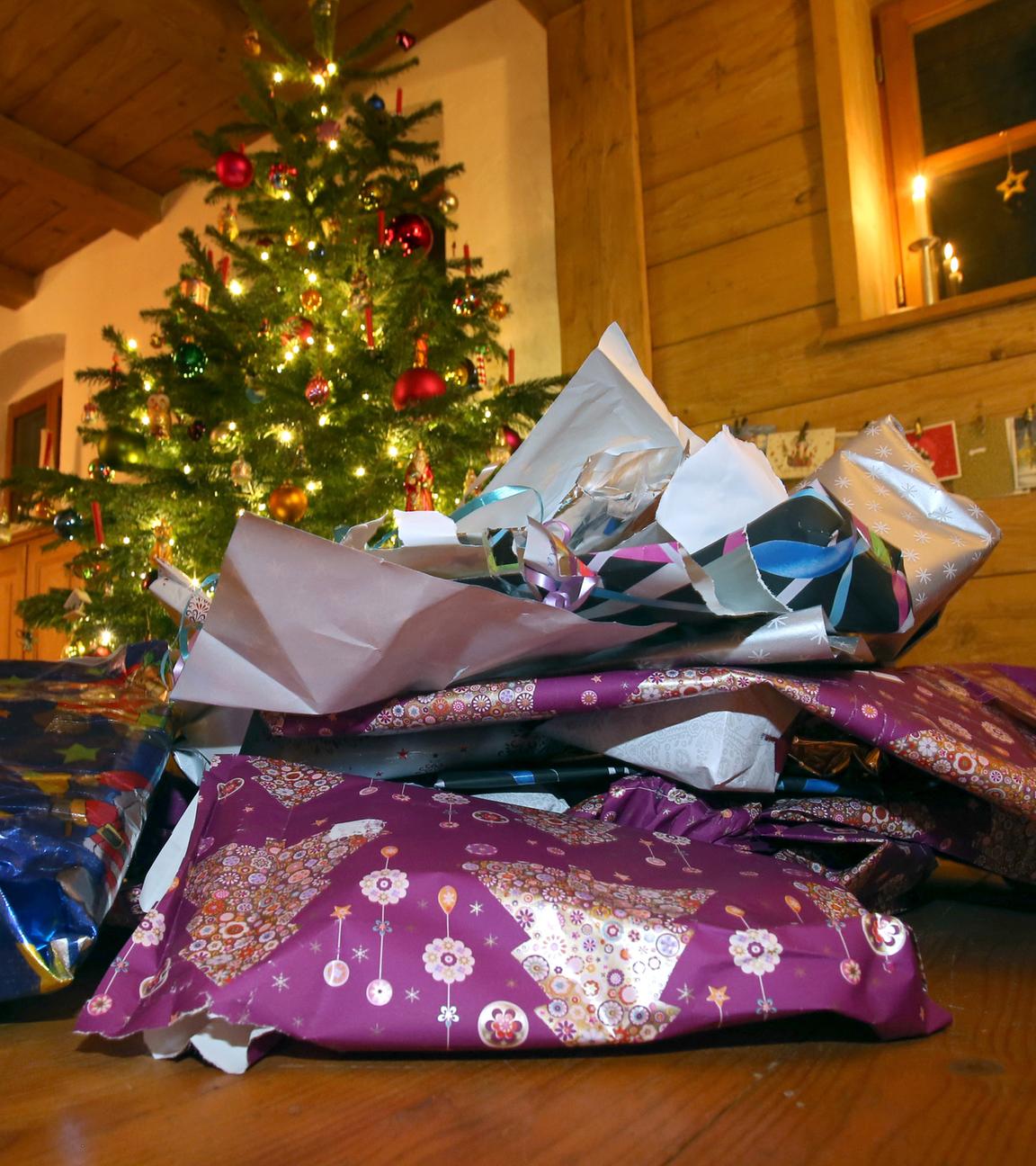 Zerknülltes weihnachtliches Geschenkpapier liegt vor einem geschmücktem Christbaum.