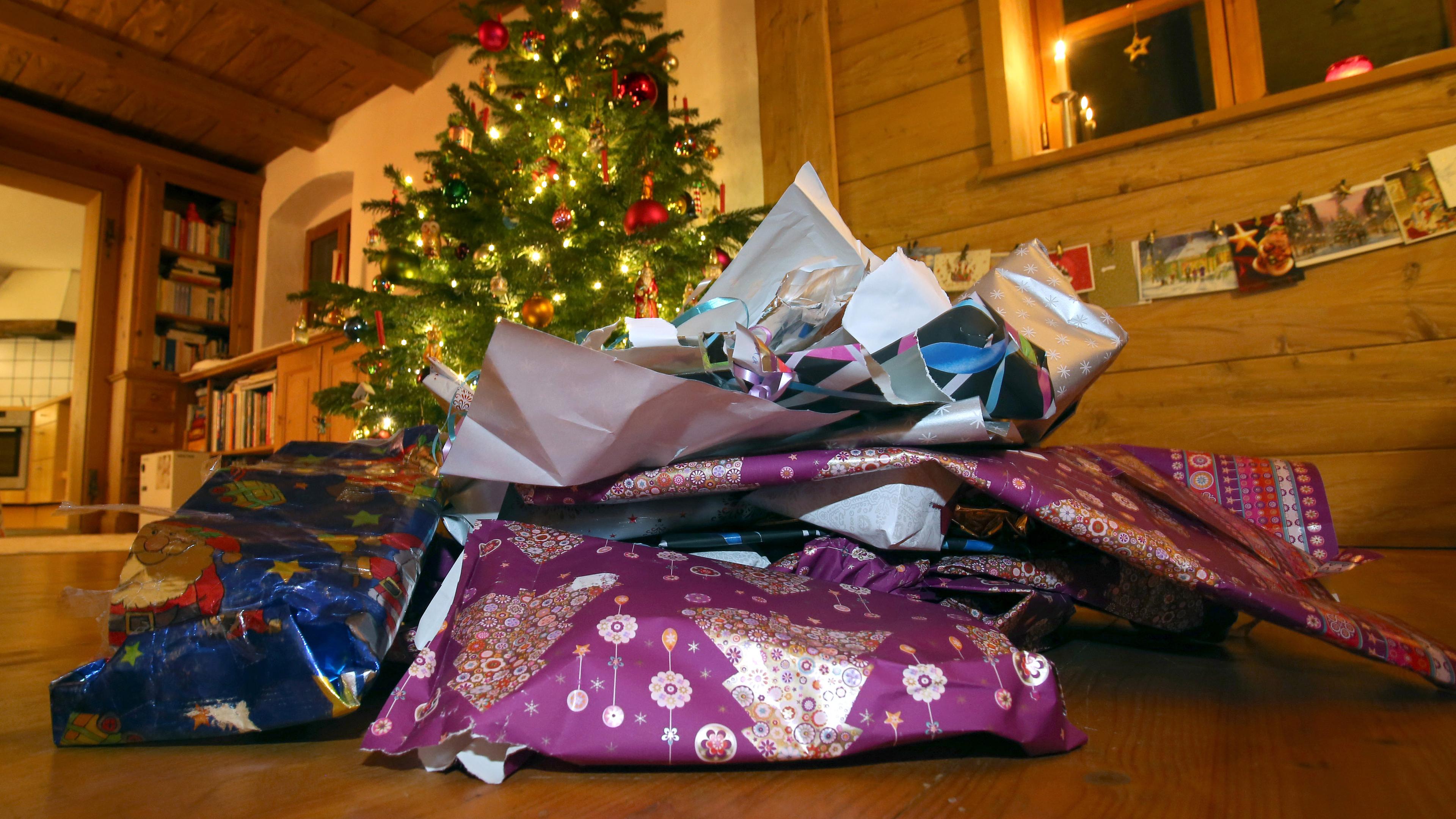 Zerknülltes weihnachtliches Geschenkpapier liegt vor einem geschmücktem Christbaum.