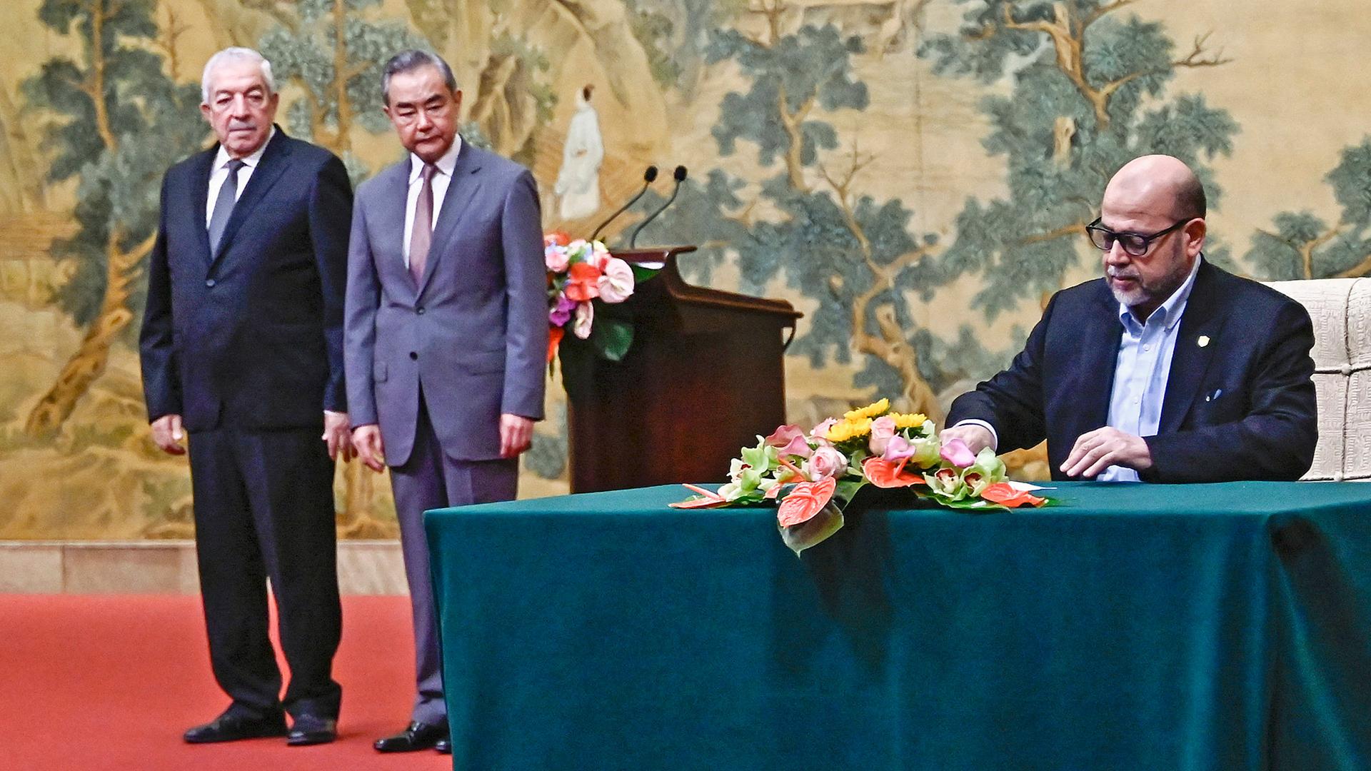 Mussa Abu Marzuk (r., Hamas), unterzeichnet ein Dokument, während Chinas Außenminister Wang Yi (2.v.l) und Mahmoud al-Aloul (Fatah) im Hintergrung zusehen sind