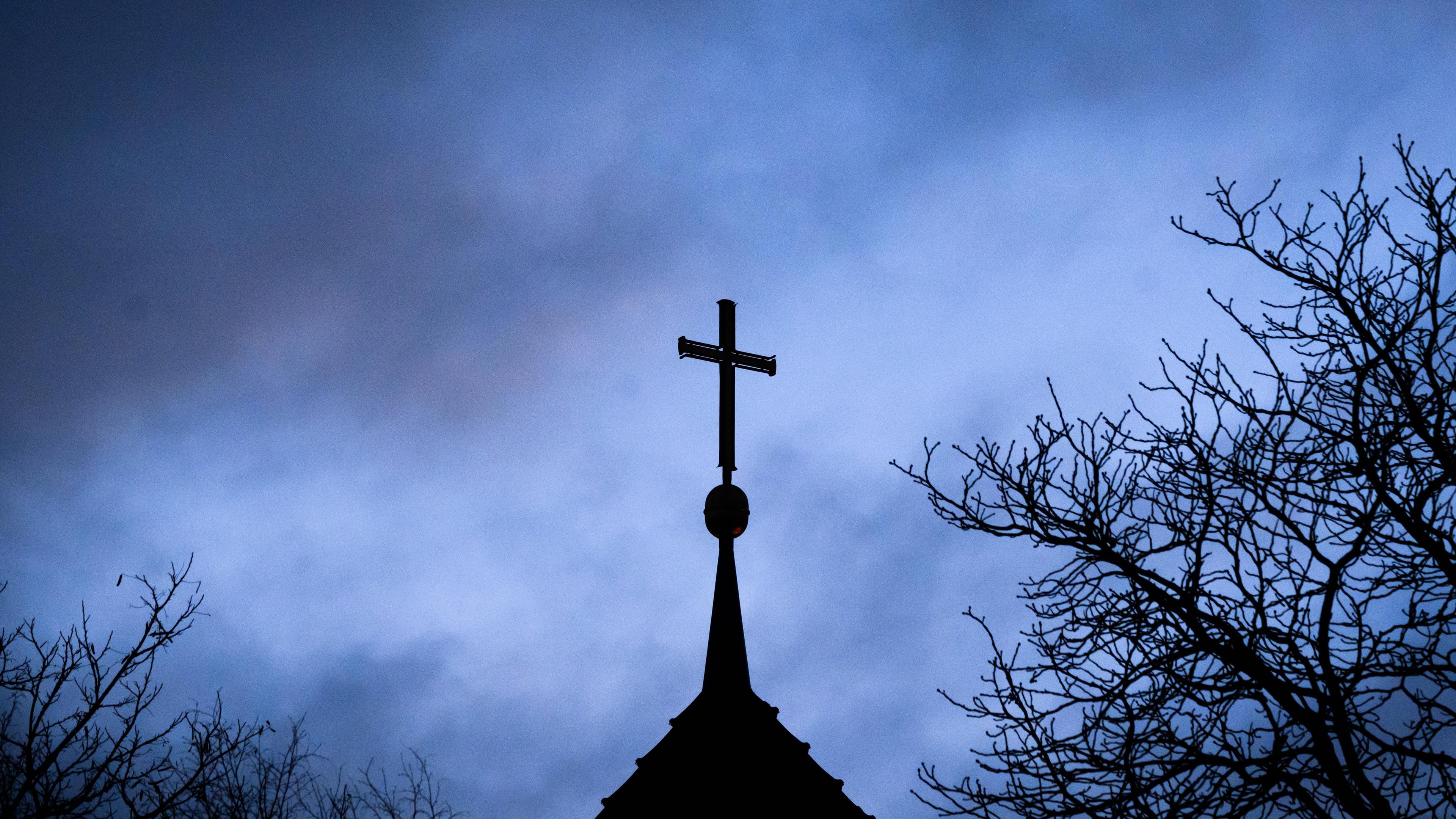 Dunkle Wolken ziehen über das Kreuz auf einer evangelischen Kirche in der Region Hannover hinweg.