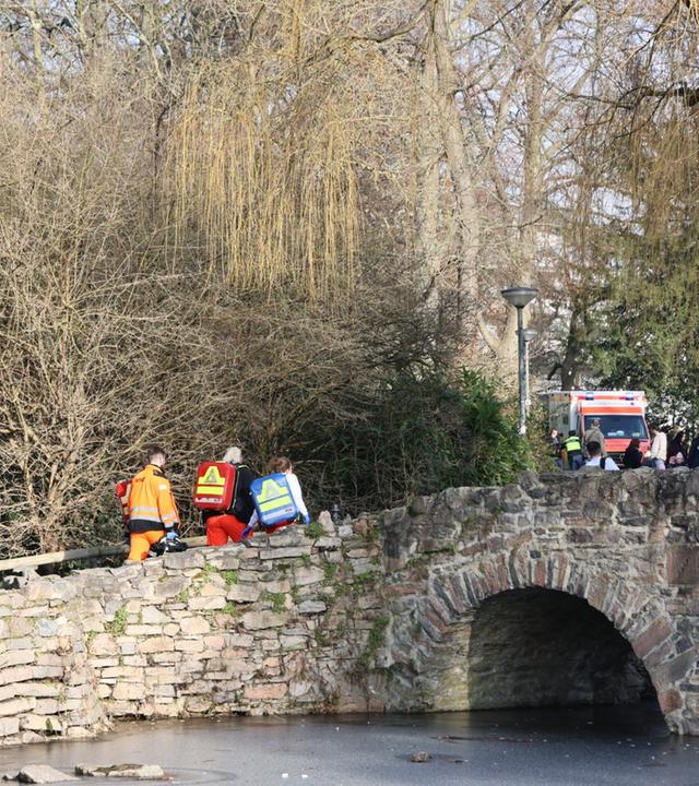 Bayern, Aschaffenburg: Rettungskräfte und Kriminaltechniker gehen in der Nähe eines Tatortes eine kleine Brücke hinauf.