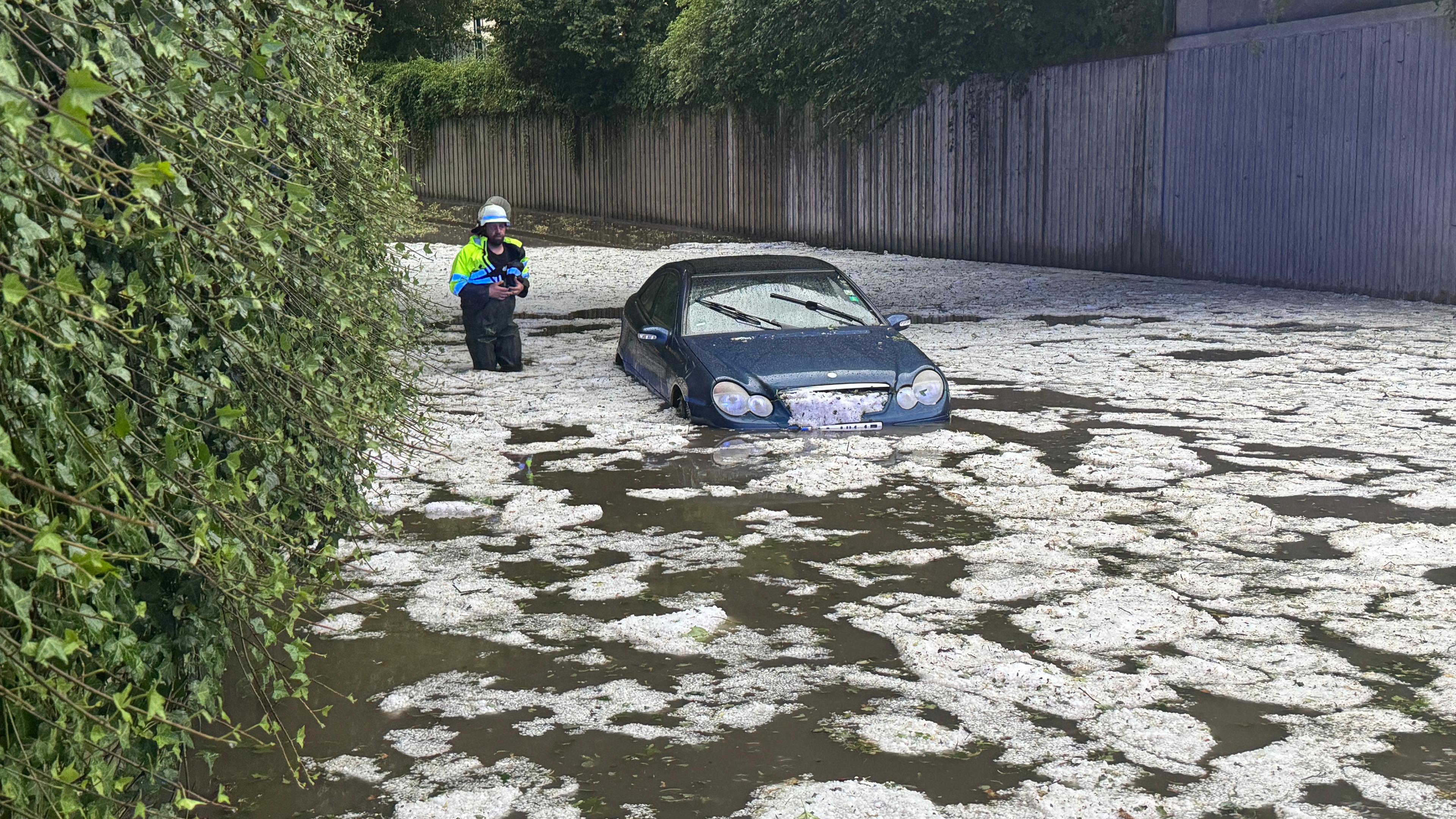 Nach schweren Unwettern steht ein Auto auf einer überfluteten Straße, in der Hagelkörner treiben.