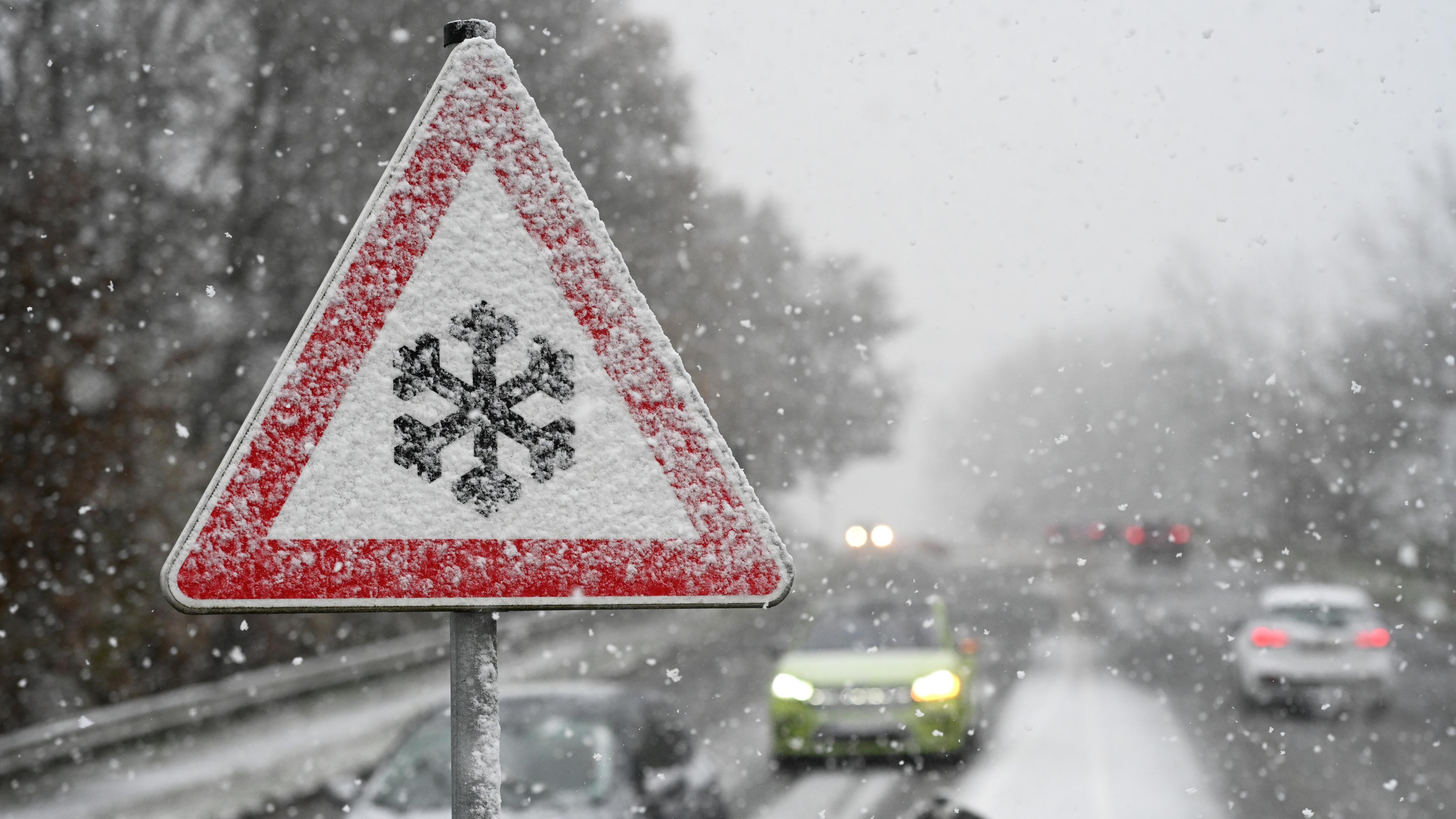 Ein Verkehrschild an der Südring-Brücke warnt vor Gefahr von Schnee- oder Eisglätte auf der Fahrbahn, während Schnee fällt.